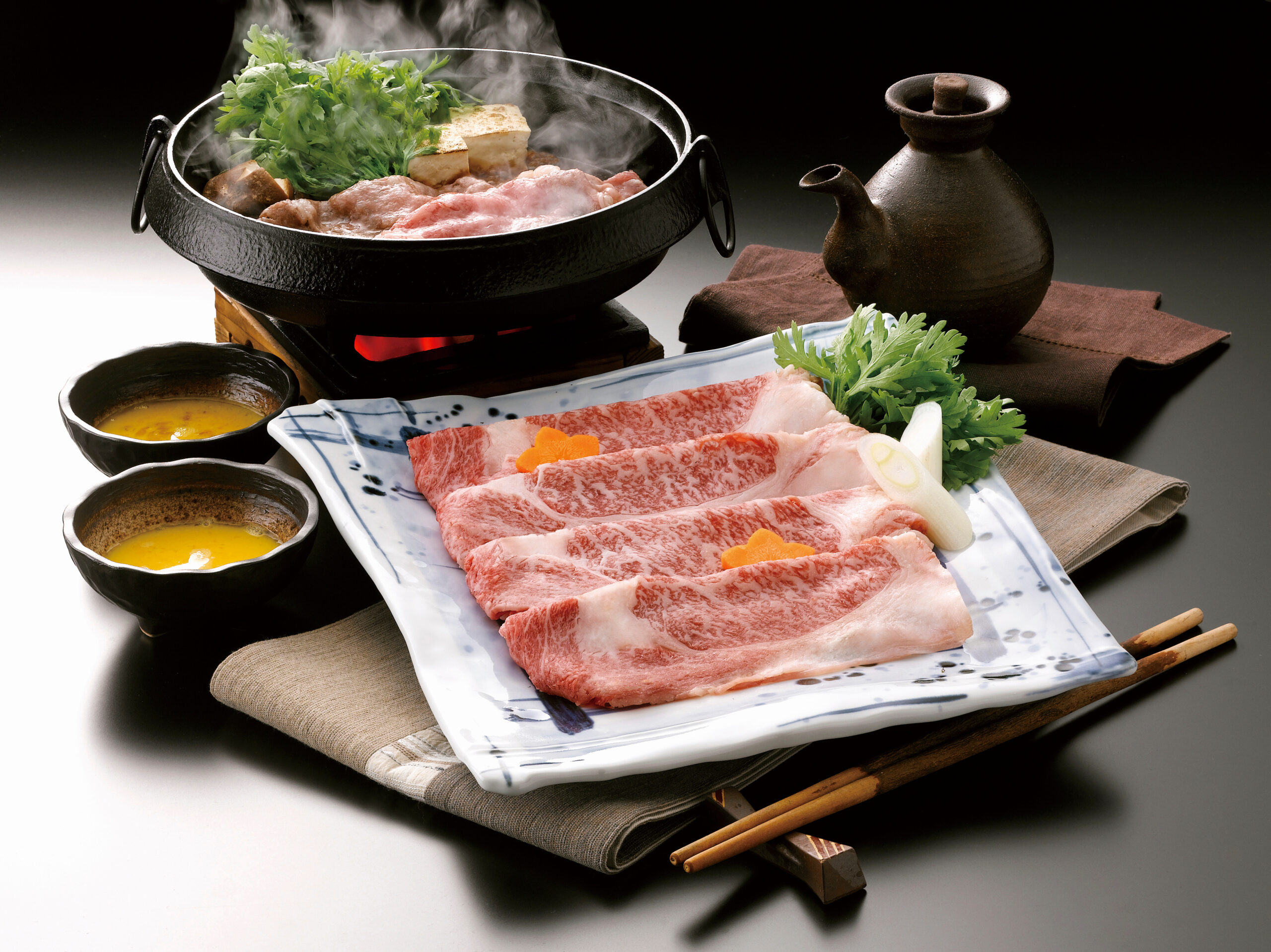 Beef slices with greens and tofu steaming in a black hot pot, with dipping bowls and chopsticks nearby.