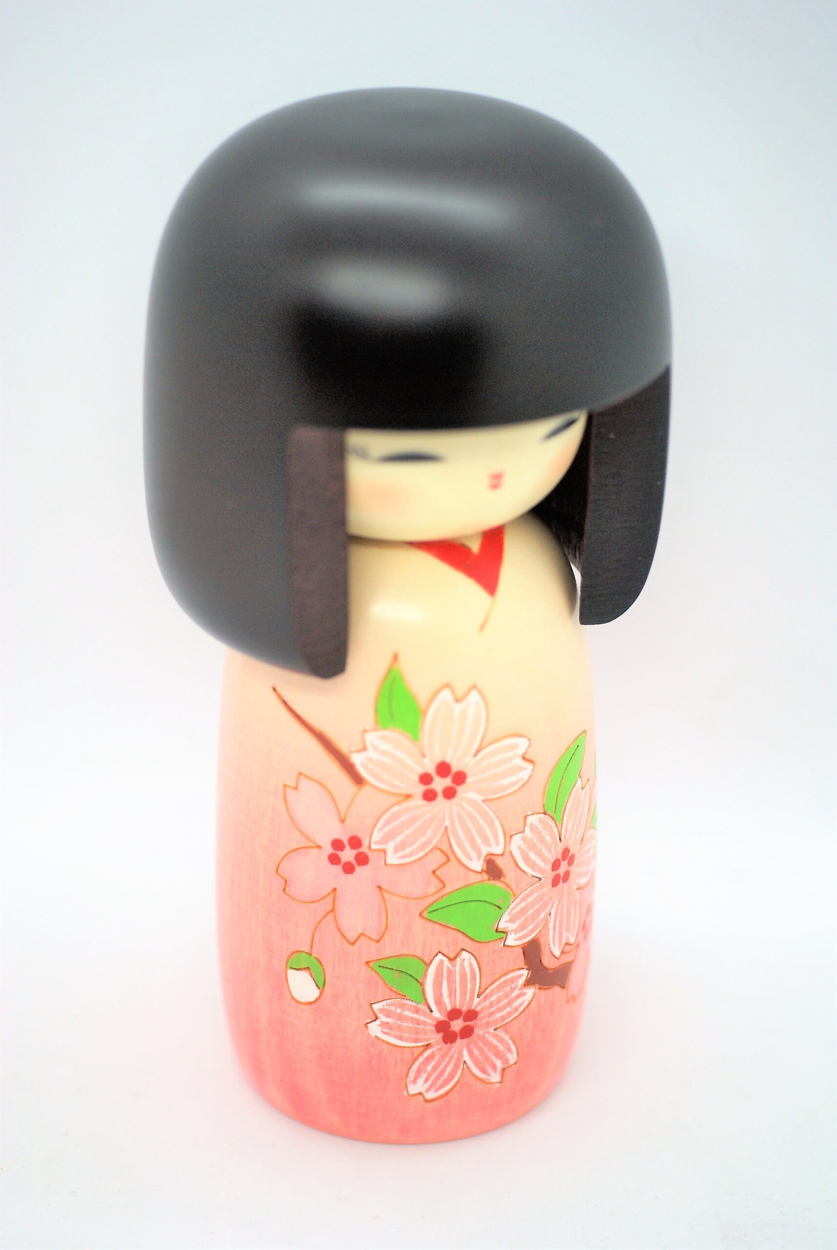 Kokeshi doll with a black bob hairstyle, pale face, and a pink floral kimono visible on the wooden body.