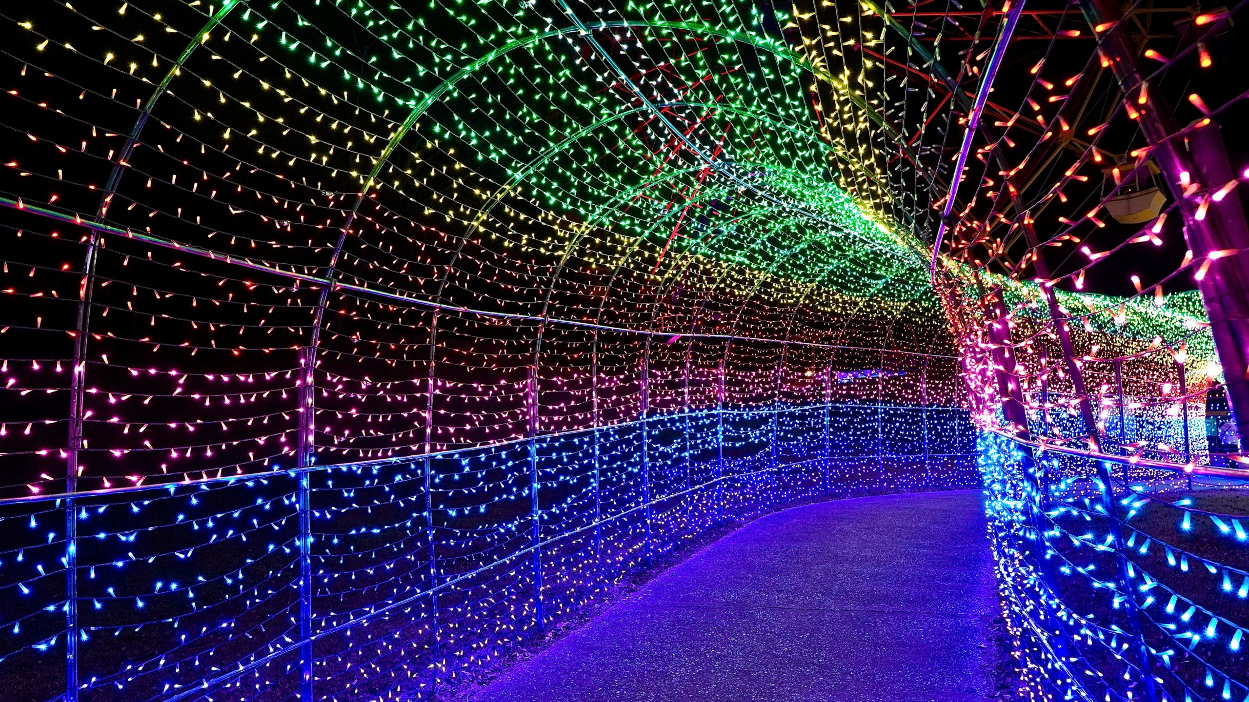 Walkway lined with rainbow-colored fairy lights forming a tunnel at night