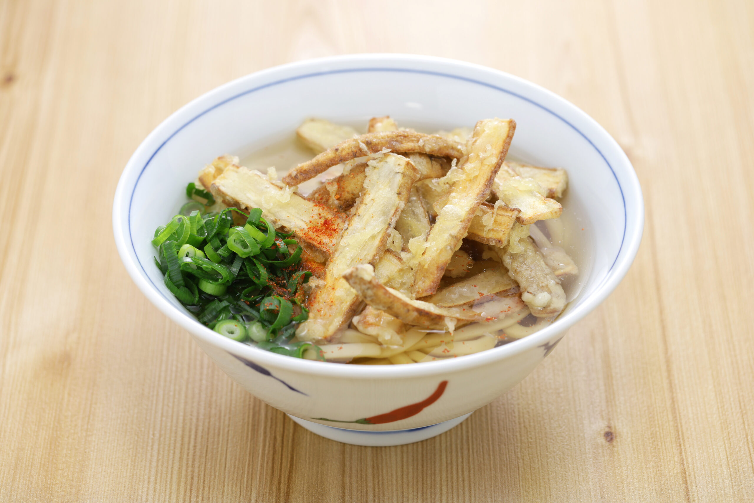 Bowl of ramen with fried tempura and sliced green onions on a wooden table.