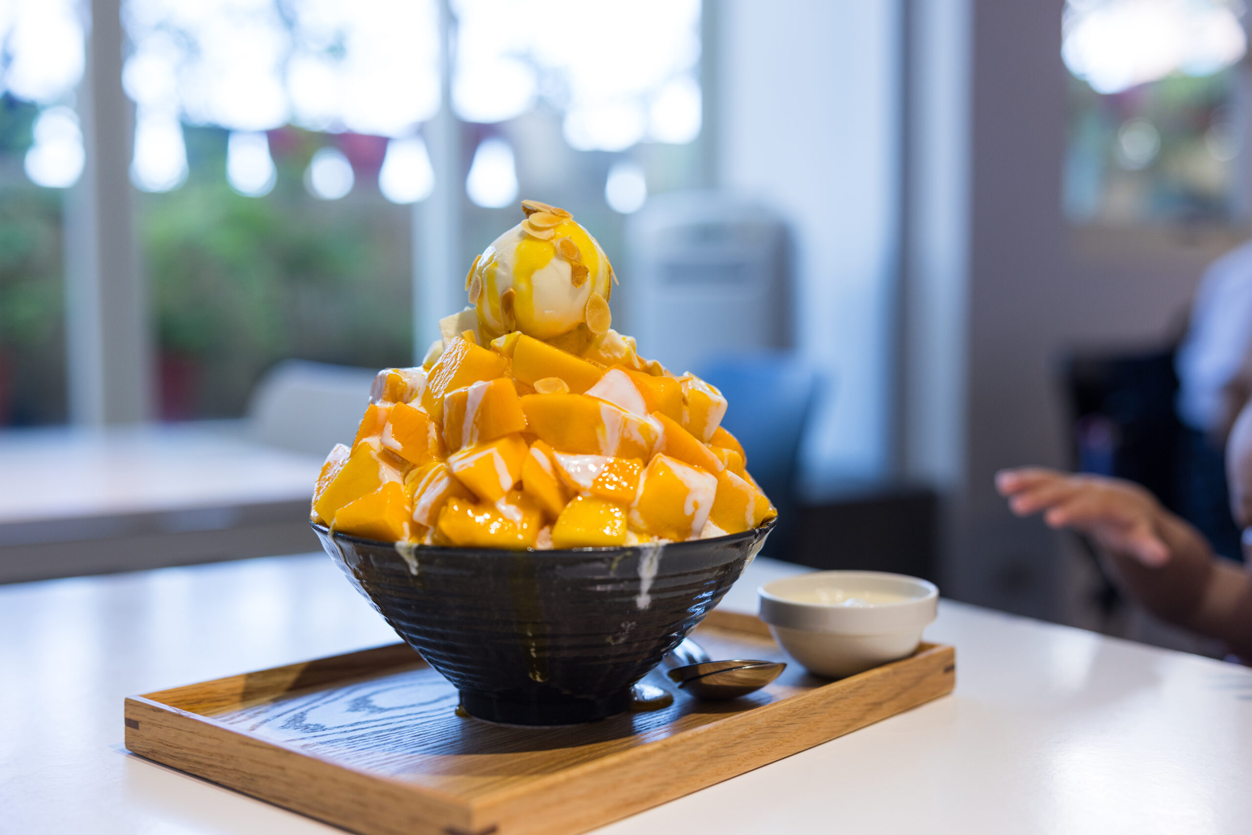 Mango dessert bowl piled with mango chunks, topped with vanilla ice cream and almond slices on a wooden tray.