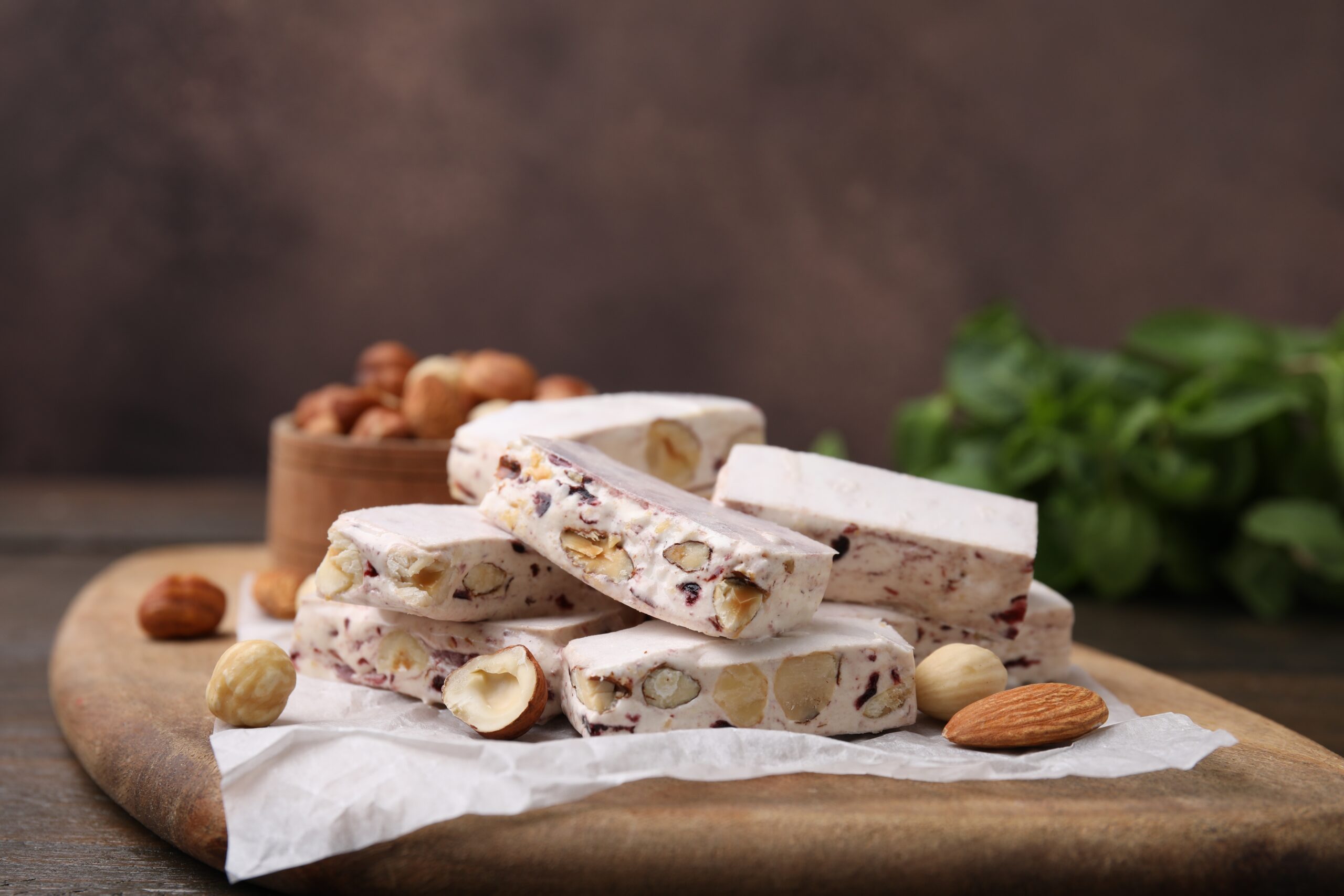 Stack of nut-filled nougat bars with almonds and hazelnuts on parchment atop a wooden board.