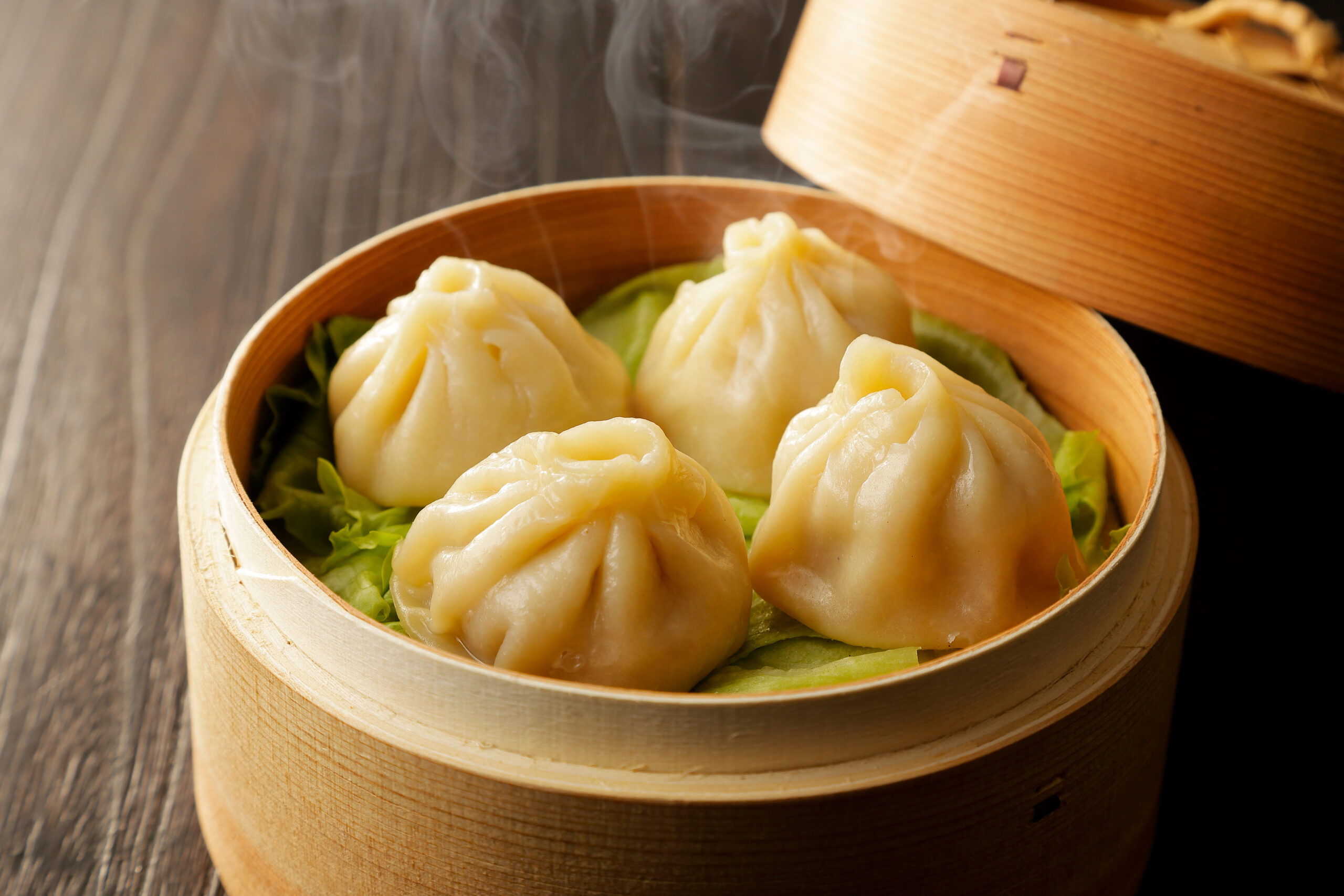 Steamer basket filled with plump steamed dumplings on a bed of lettuce, resting on a wooden table.