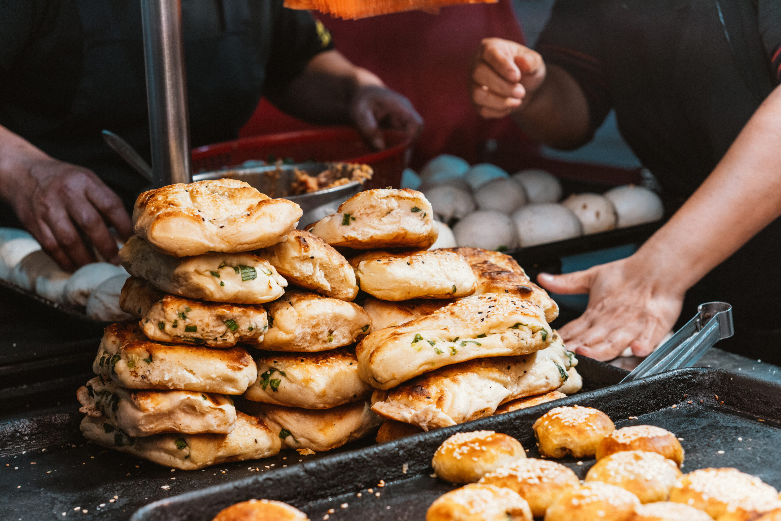 Stack of herb-garlic flatbreads stacked on a grill at a busy food stall