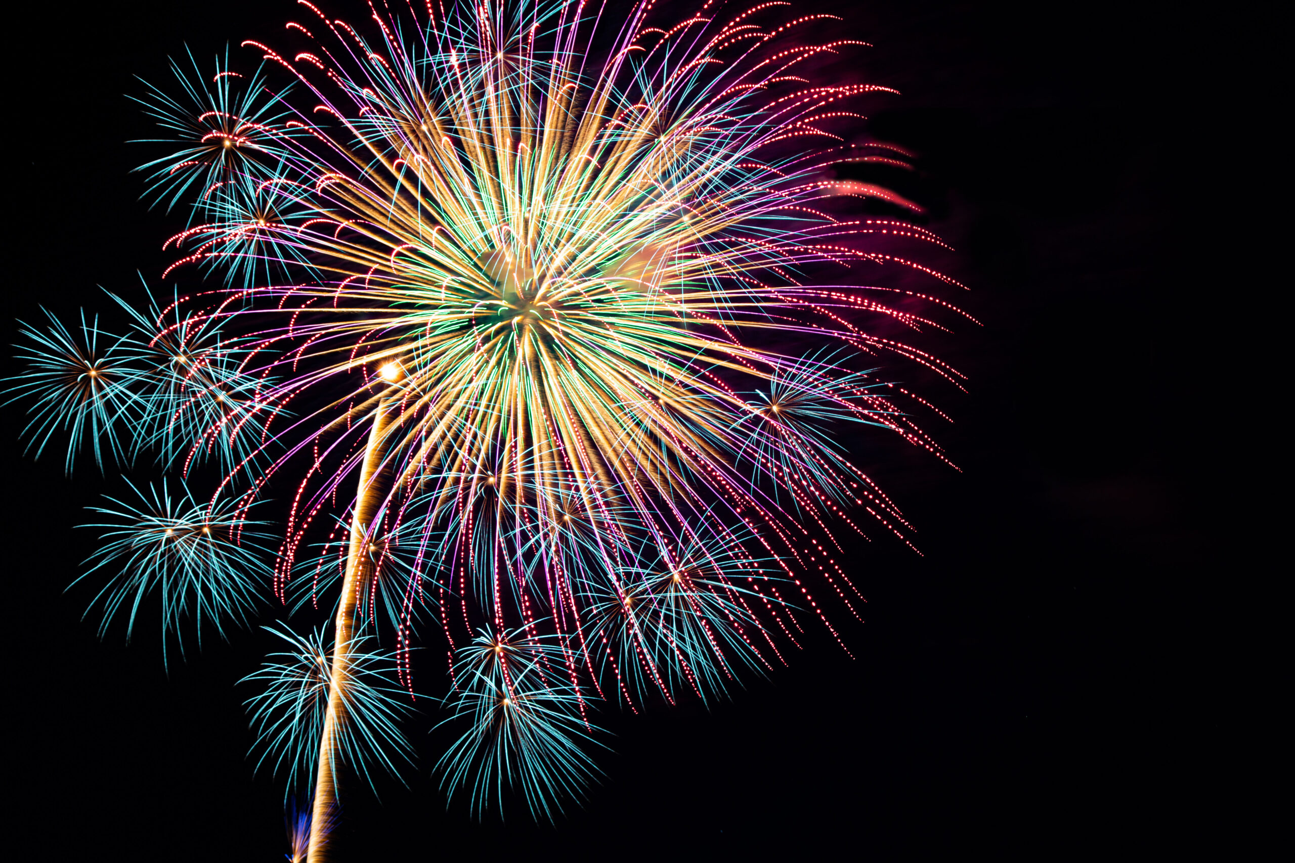 Large multicolored fireworks bursting in the night sky with blue, green, and pink trails.