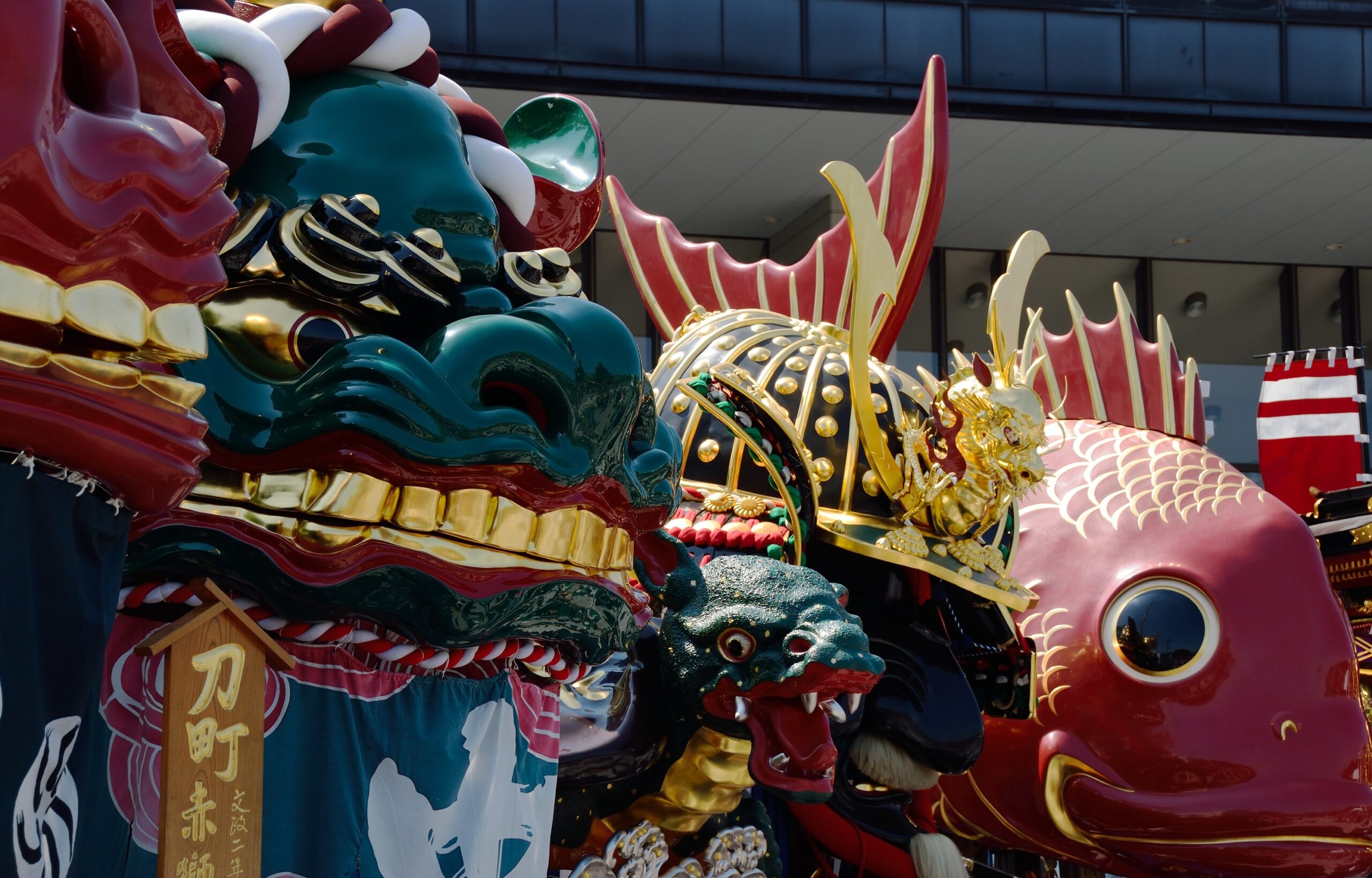 Colorful Chinese dragon parade floats with red, gold, and teal scales in an urban setting.