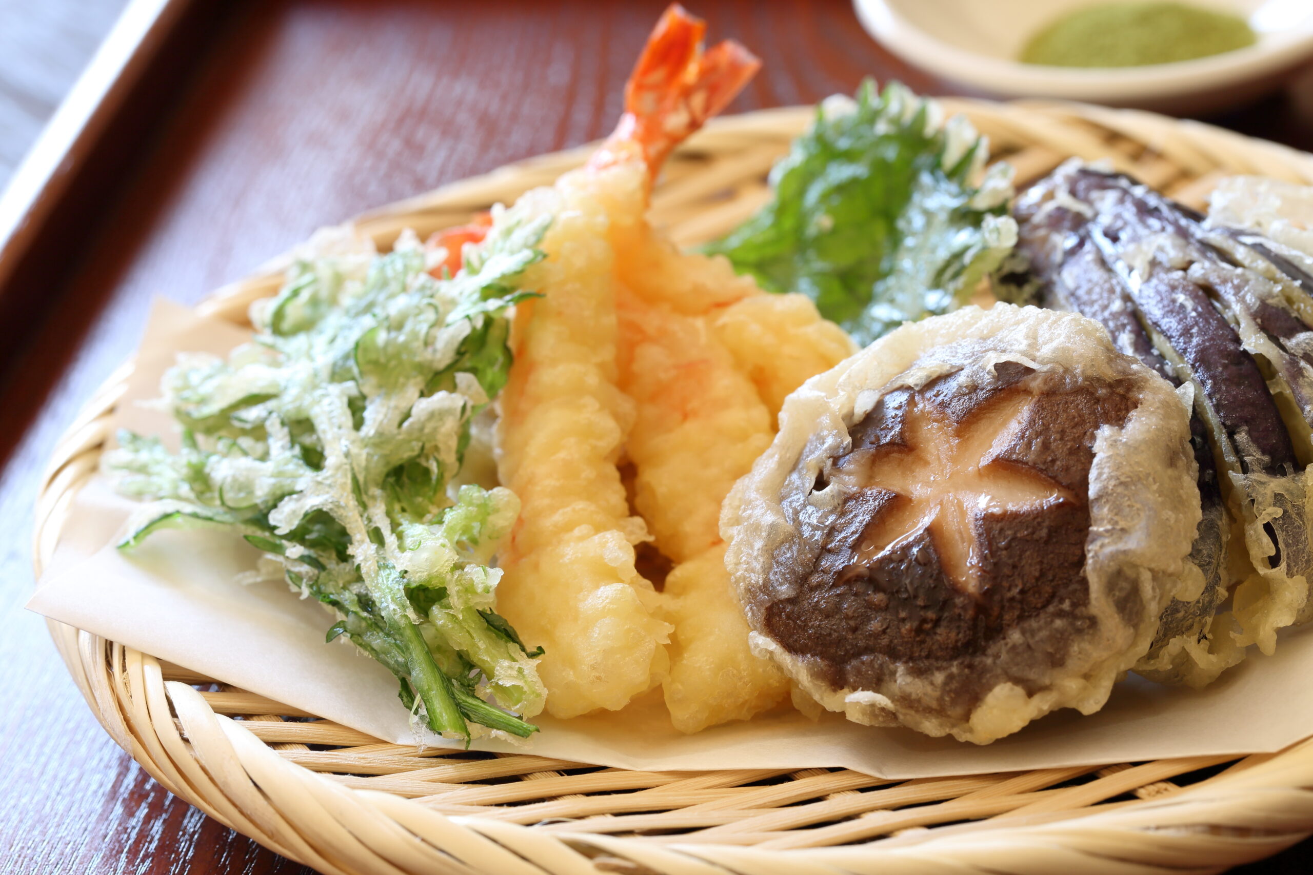 Assorted tempura (shrimp, greens, and vegetables) in a basket with paper lining.