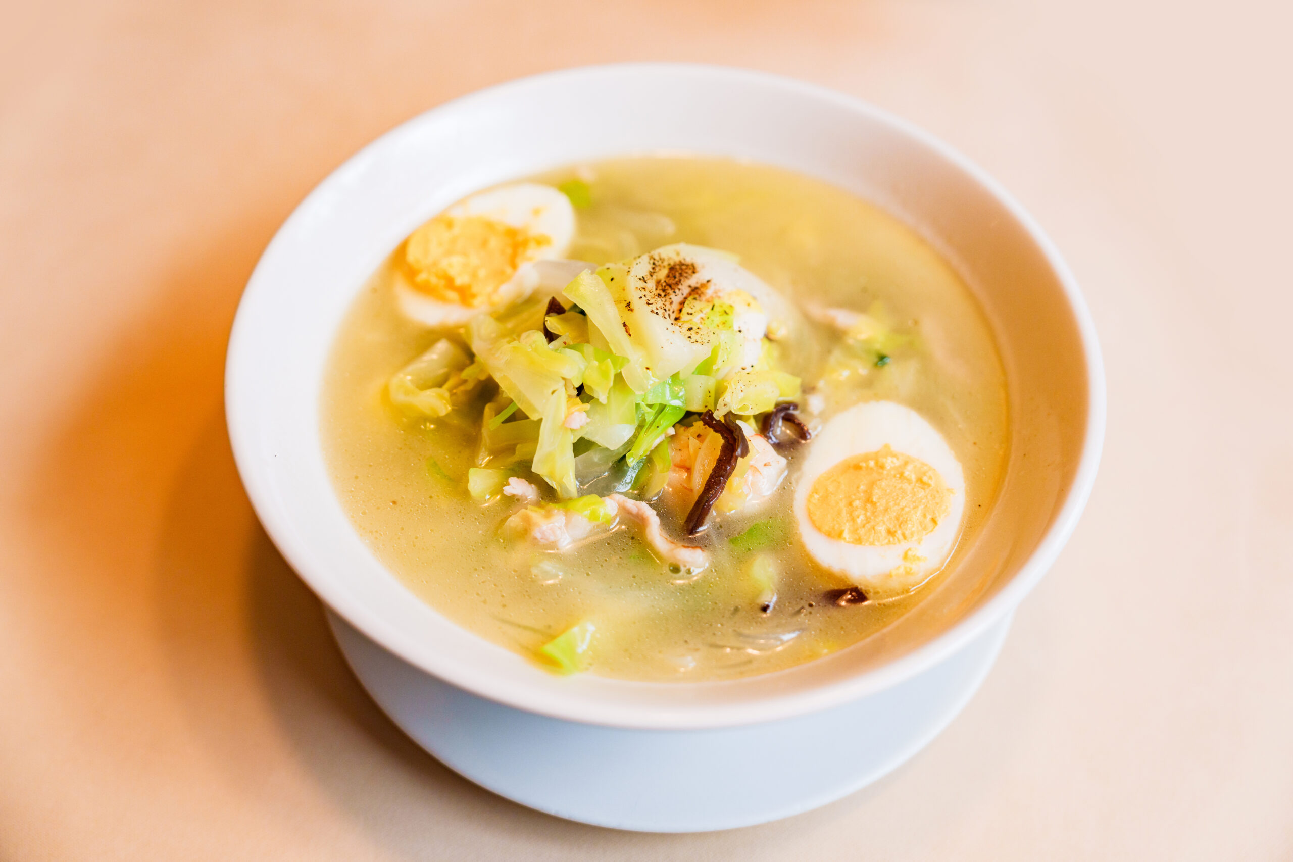 Creamy soup in a white bowl topped with halved hard-boiled eggs, shredded cabbage, and green onions.