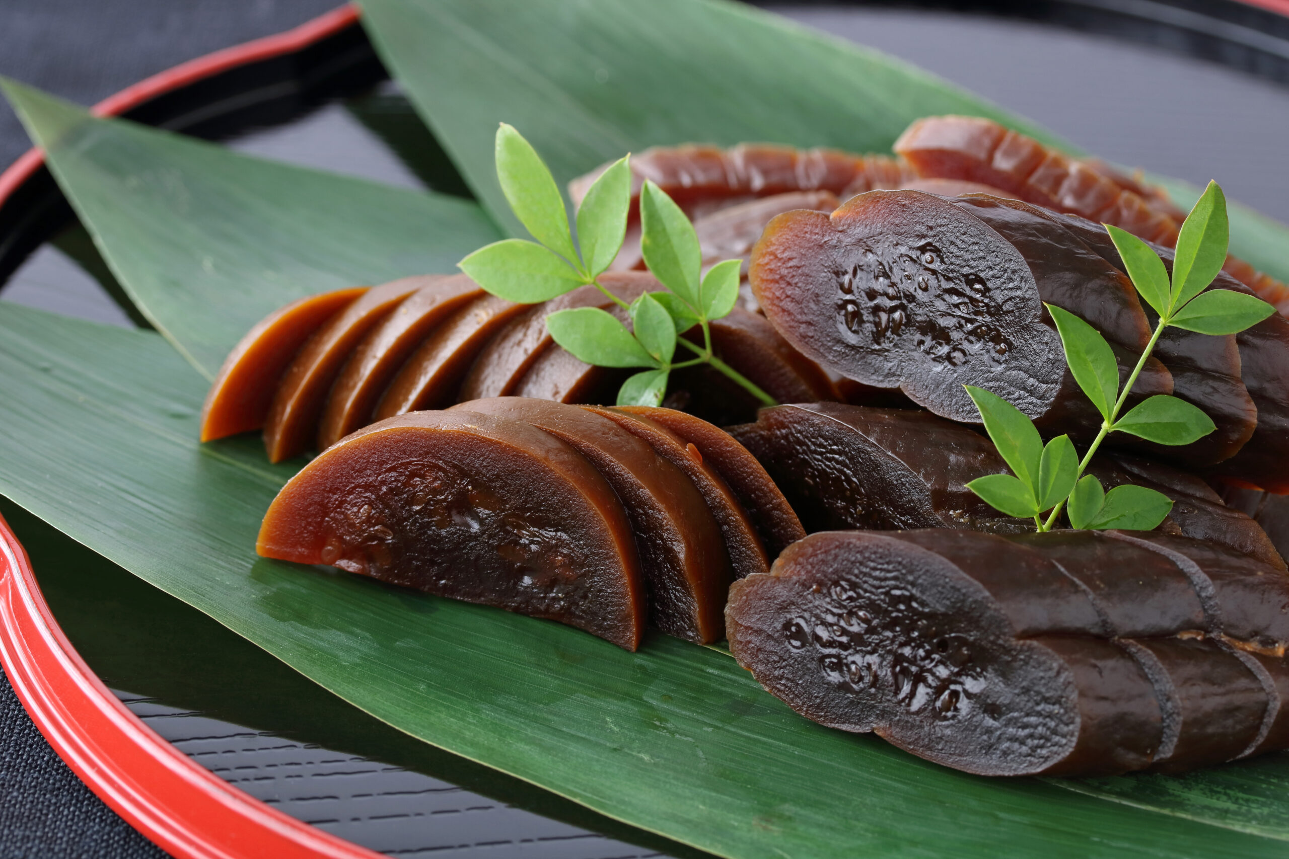 Slices of dark brown jelly arranged on a banana leaf with small green sprigs as garnish on a red-rimmed plate