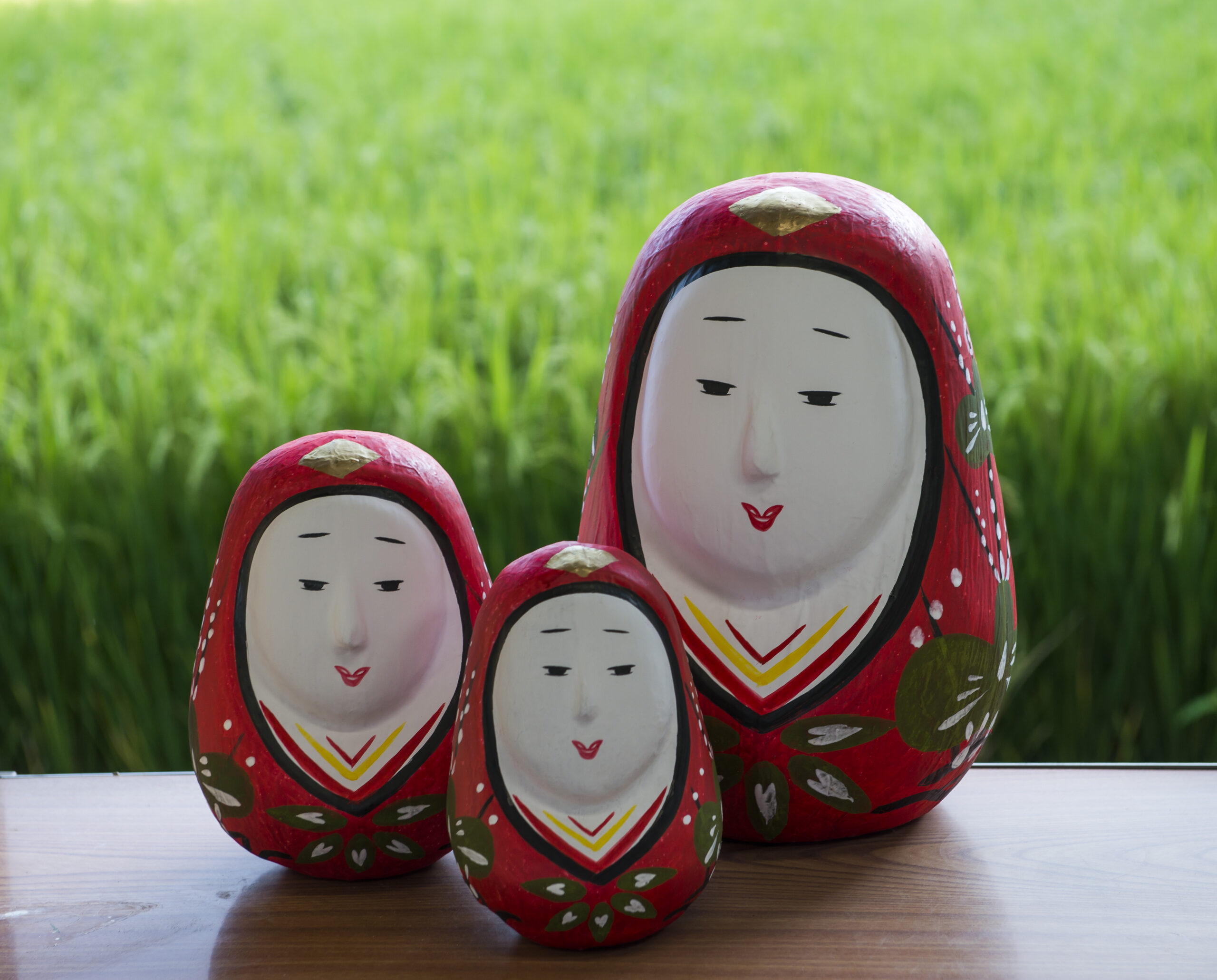 Set of red Matryoshka nesting dolls on a wooden table with a green grassy background.