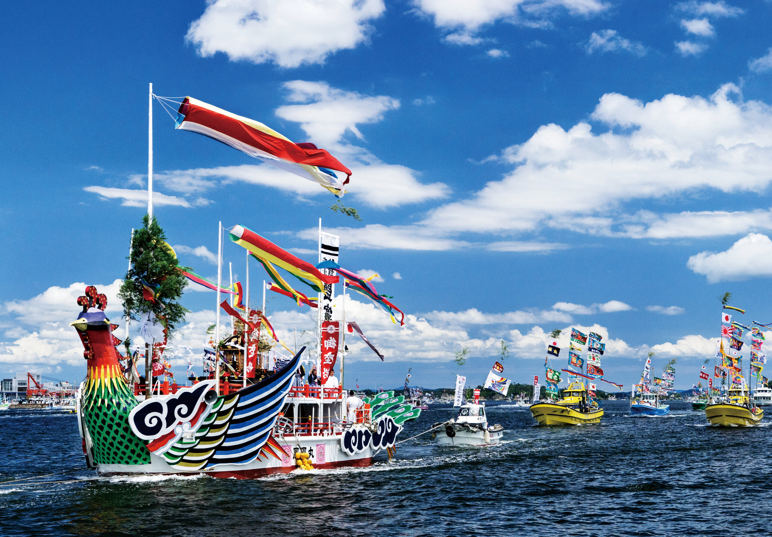 Colorful festival boat with a dragon-like prow and fluttering banners on a calm harbor under a blue sky, amid other festive boats and flags.