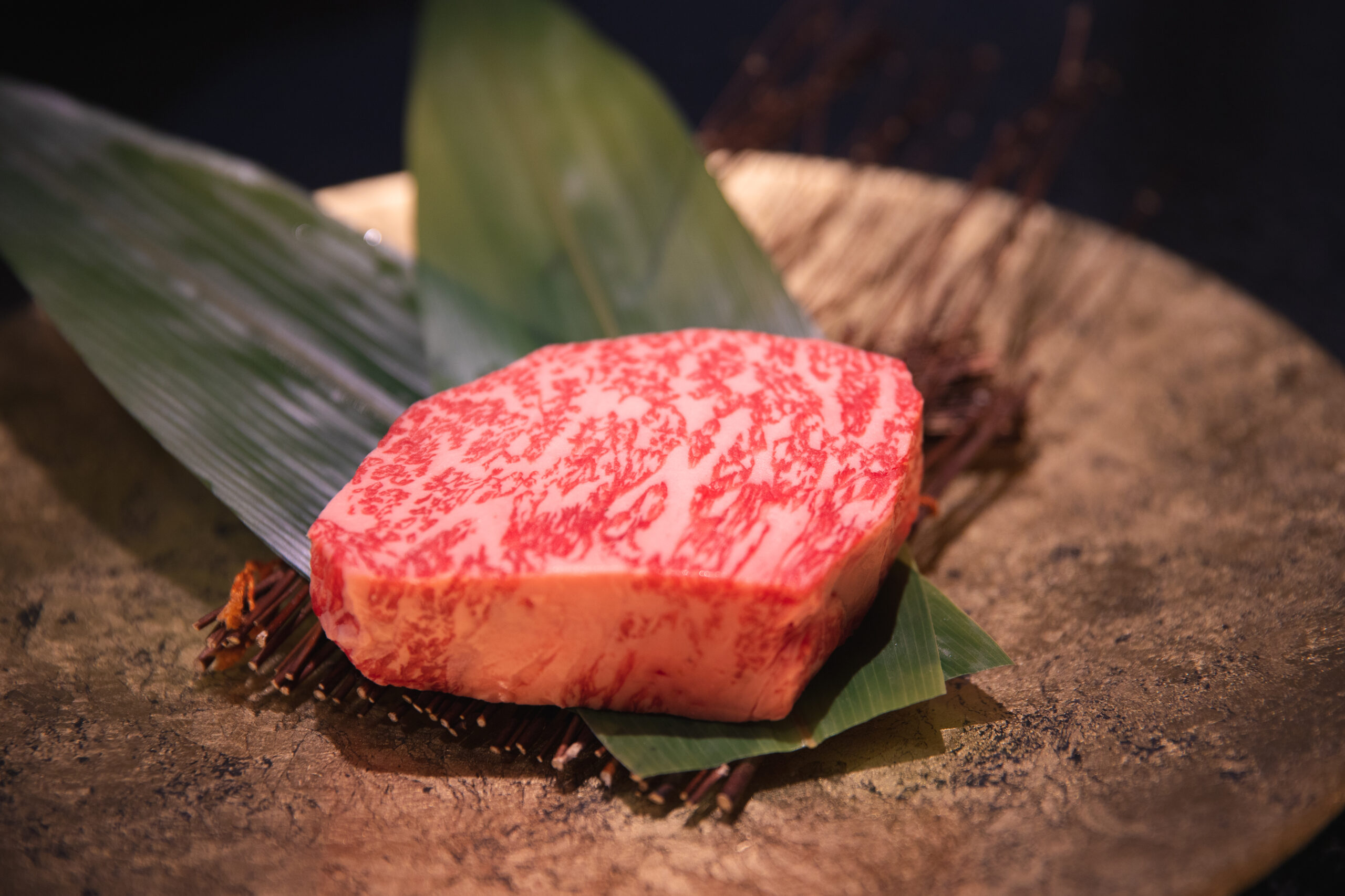 Thinly sliced marbled Wagyu beef resting on a green leaf over a stone surface (close-up).