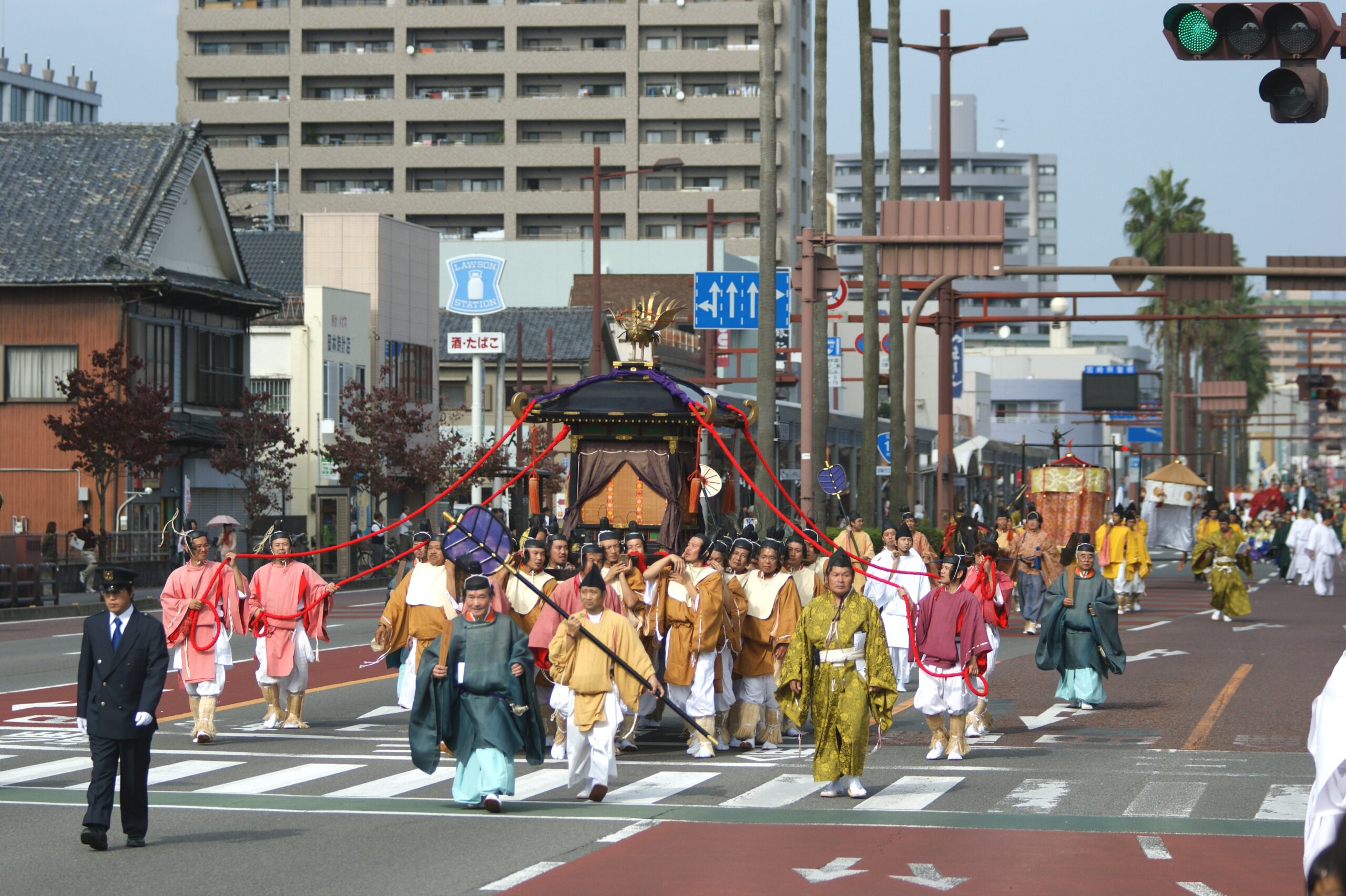 Participants in colorful traditional costumes parade down a busy city street during a festival.