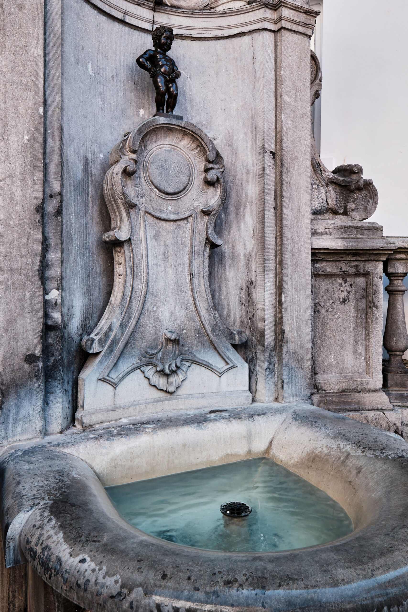 Stone fountain with a small cherub statue atop an ornate carved pedestal, weathered by time.