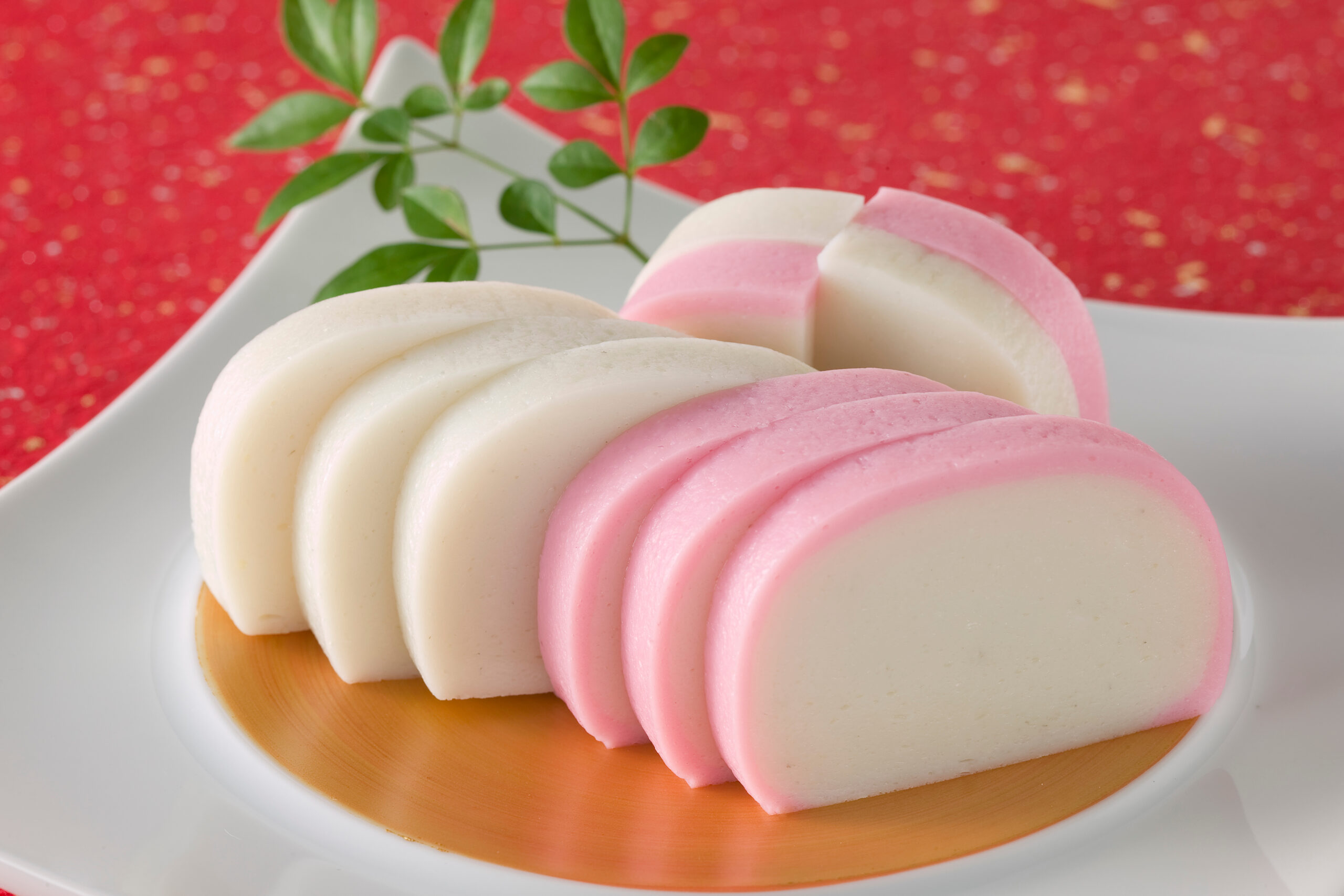 Pastel pink and white swirled marshmallows on a white plate with a green garnish against a red glittery background.