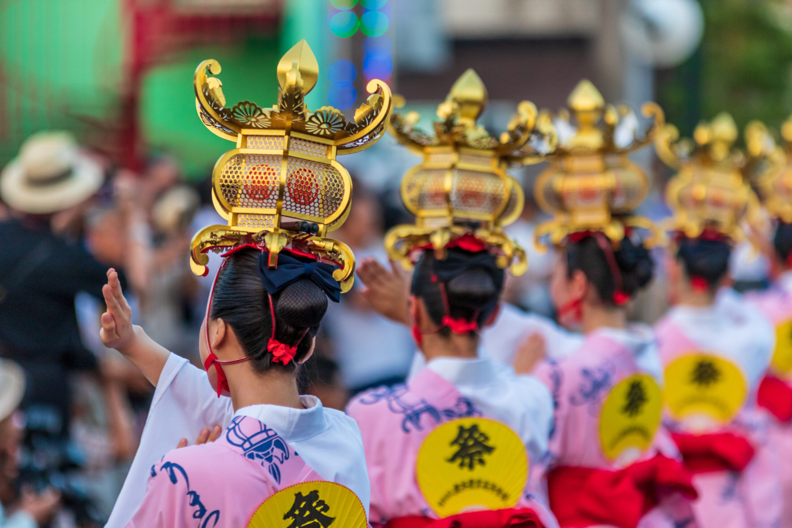 Dancers in pink outfits with tall gold ceremonial crowns perform in a street parade.