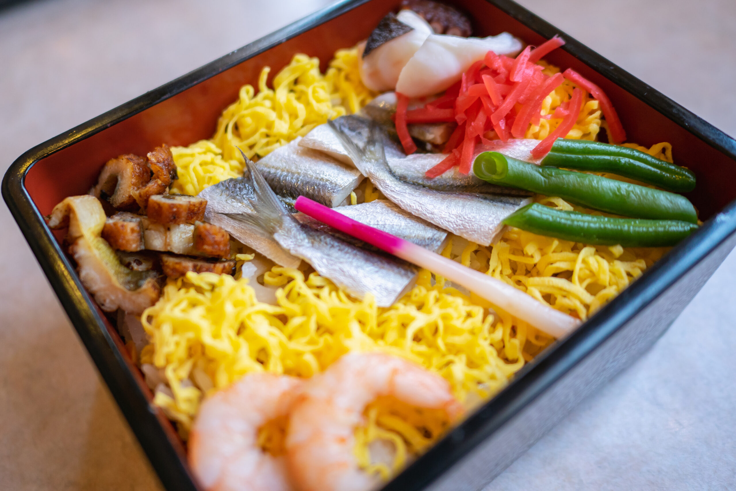 Bento box with shredded yellow egg omelette, sliced silver fish, pink pickled ginger, and green beans.