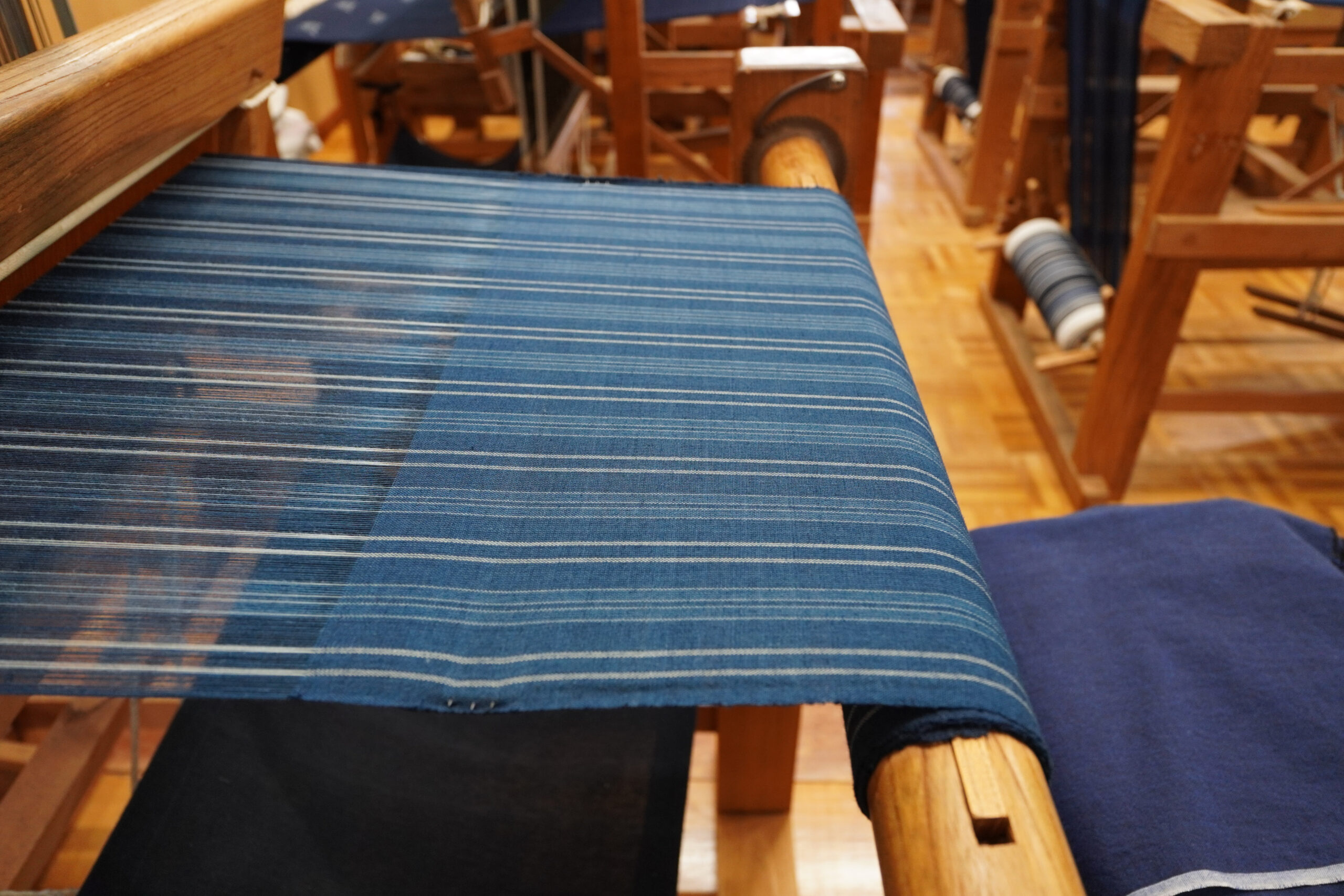 Close-up of a blue striped textile woven on a wooden loom inside a weaving studio.