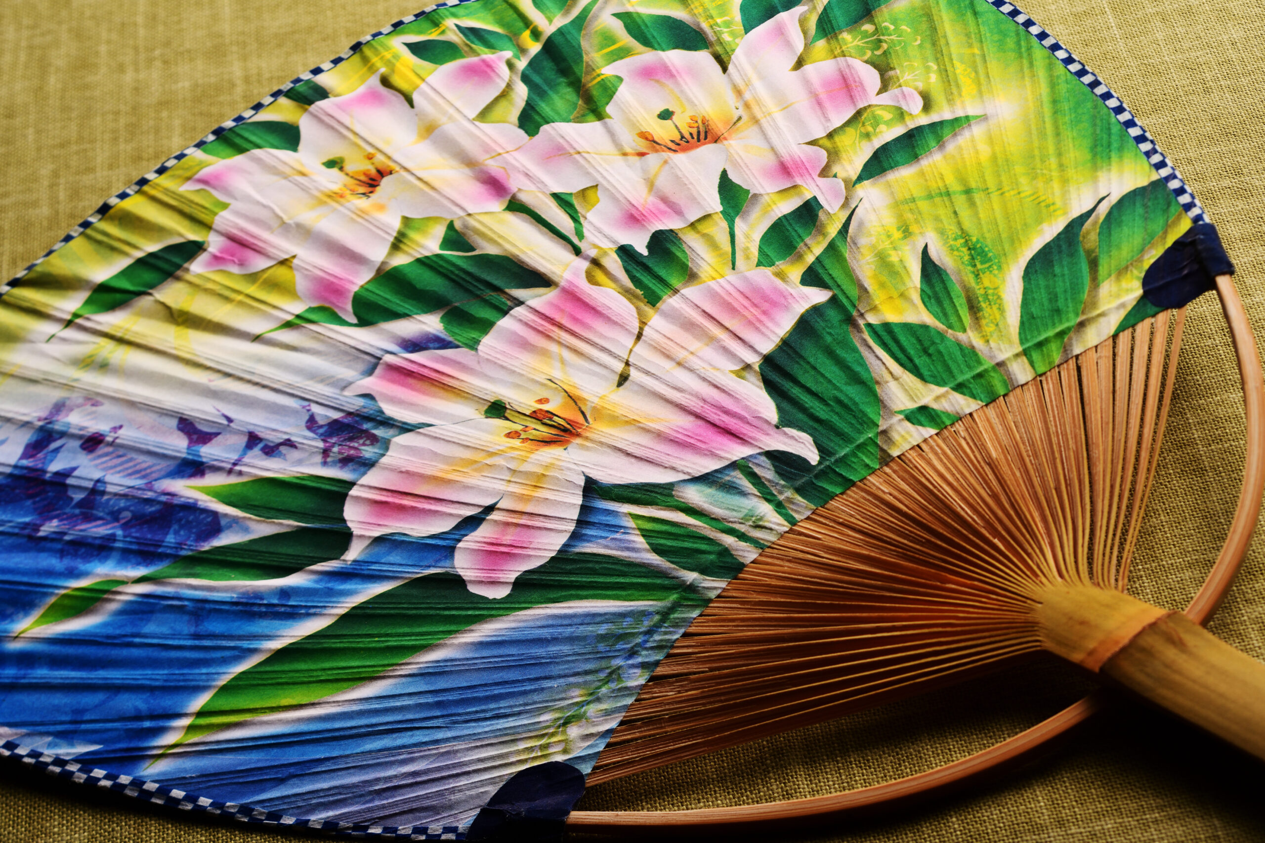 Colorful folding hand fan with pink flowers and green leaves, exposed wooden ribs at the base.