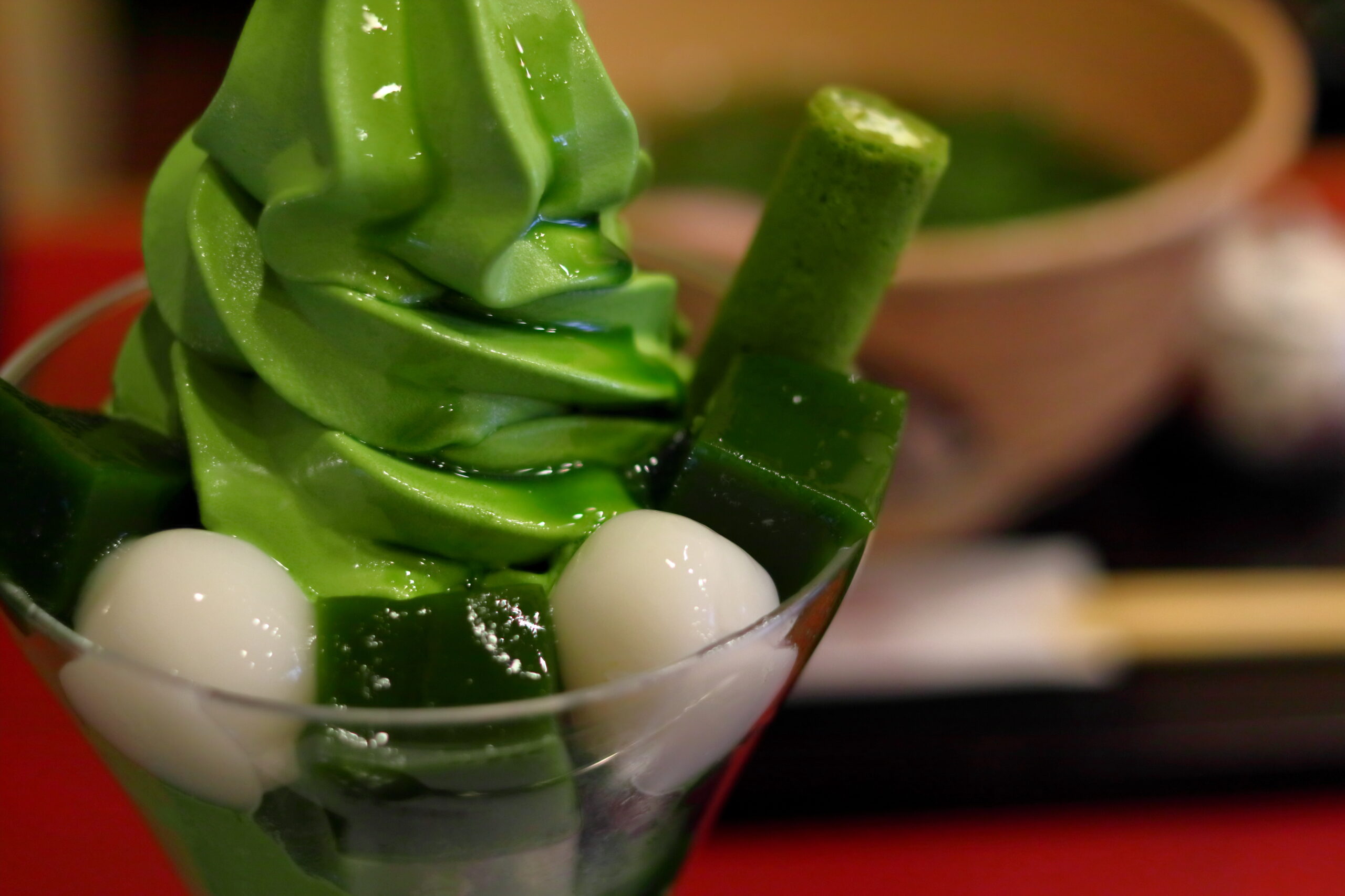 Close-up of a green matcha dessert swirled into a tall spiral in a glass, with white mochi balls at the base.