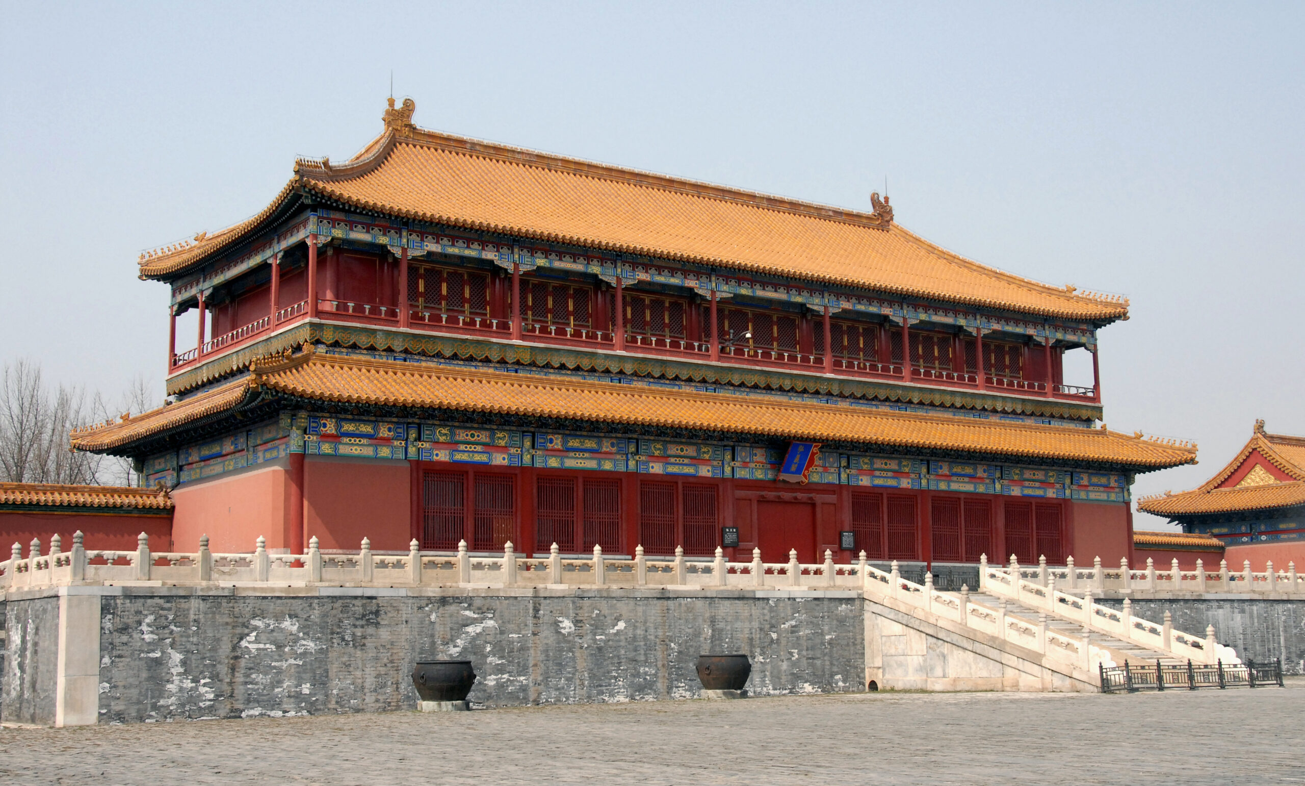 Traditional Chinese imperial building with a bright orange tiled roof, red walls, and decorative blue trim on a stone courtyard setting.