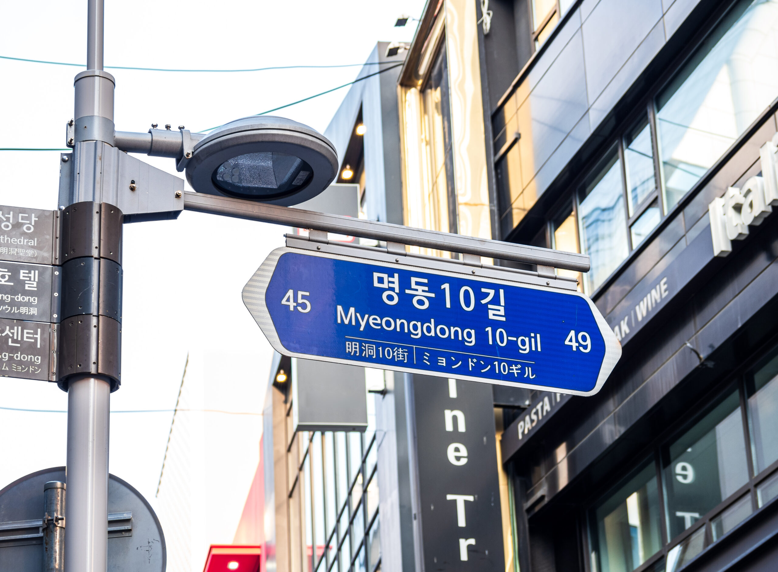 Blue street sign reading 'Myeongdong 10-gil' with number 45, mounted on a metal pole near a glass-fronted building.