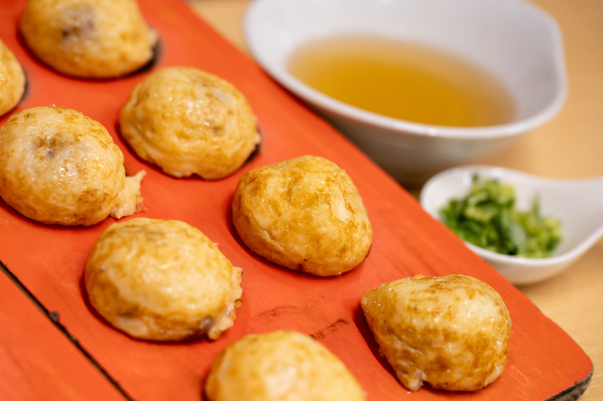 Small browned meatballs arranged on a red serving tray with dipping sauce in the background.