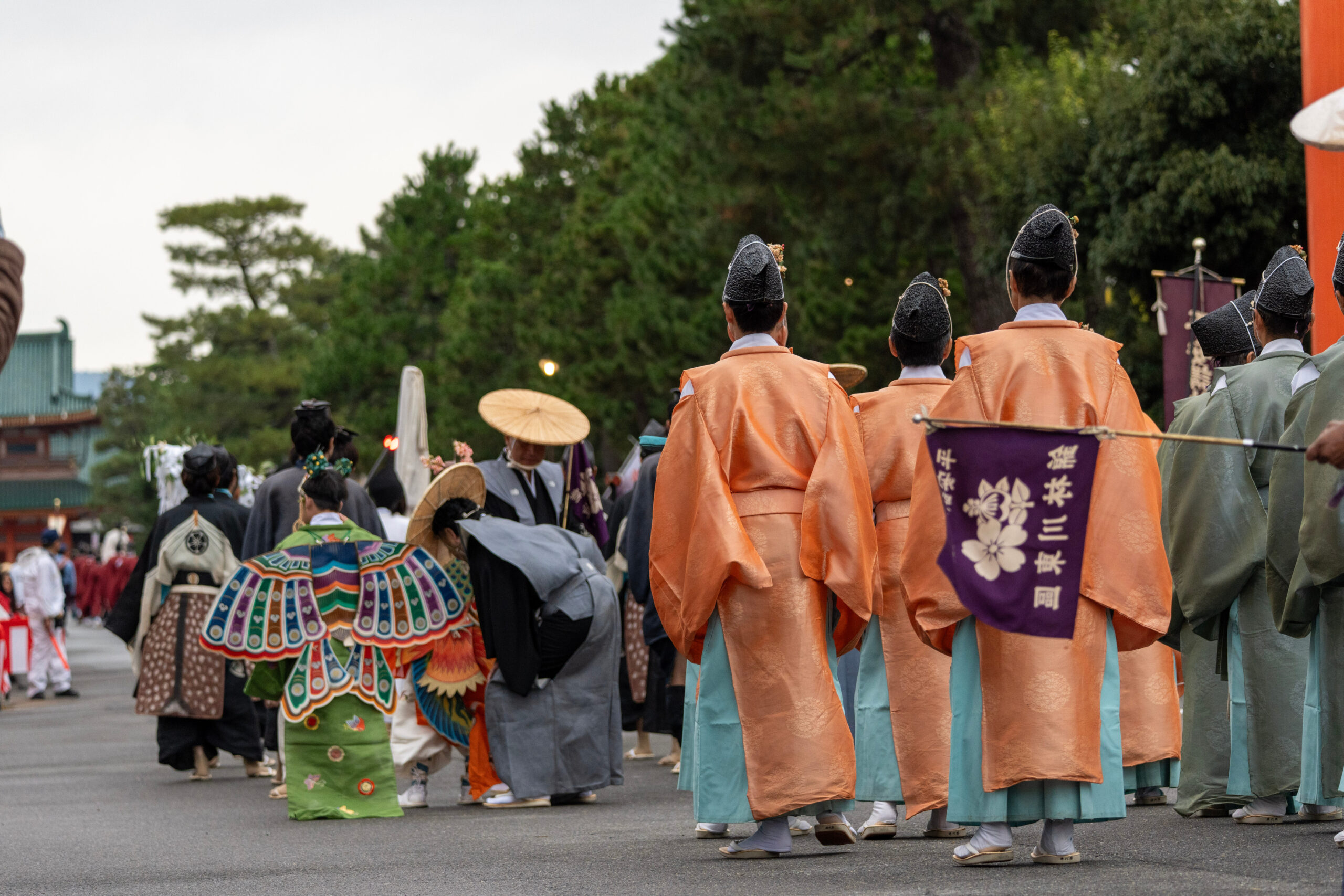 Group of performers in colorful traditional robes walking in a festival, seen from behind.