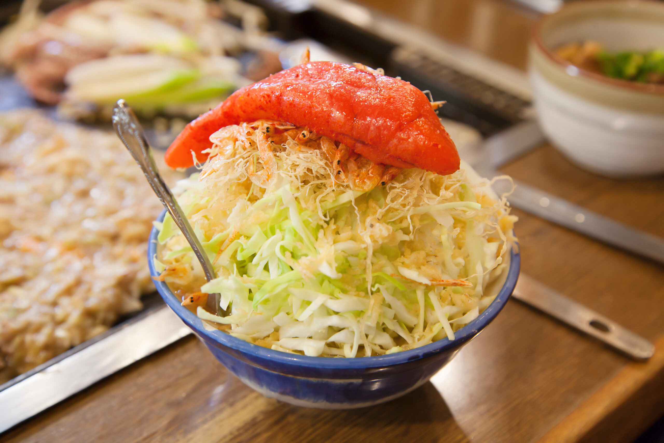 Blue bowl filled with shredded cabbage topped by lobster meat at a buffet setting.