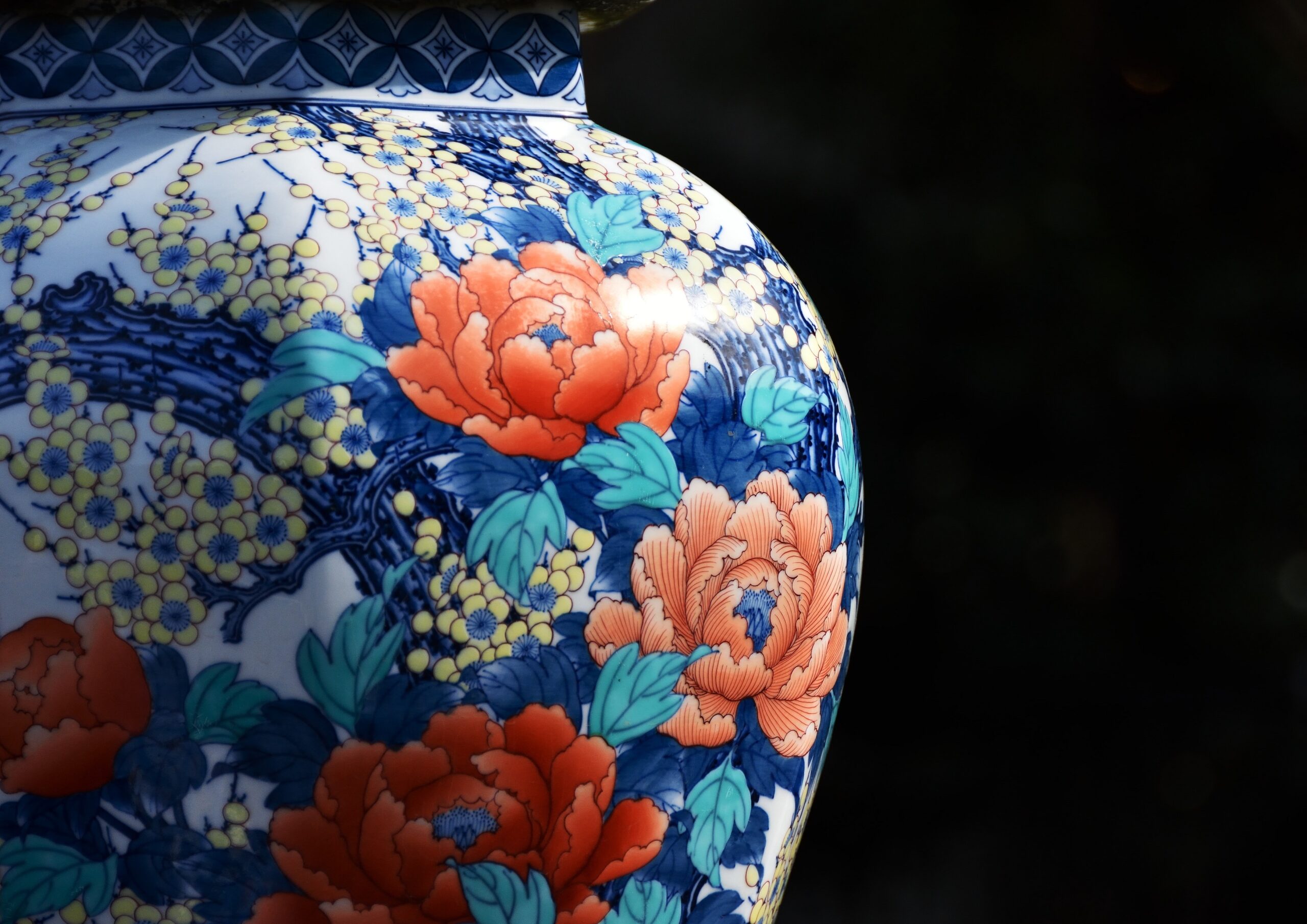 Close-up of a porcelain vase with blue and yellow floral patterns and orange flowers on white ceramic surface.