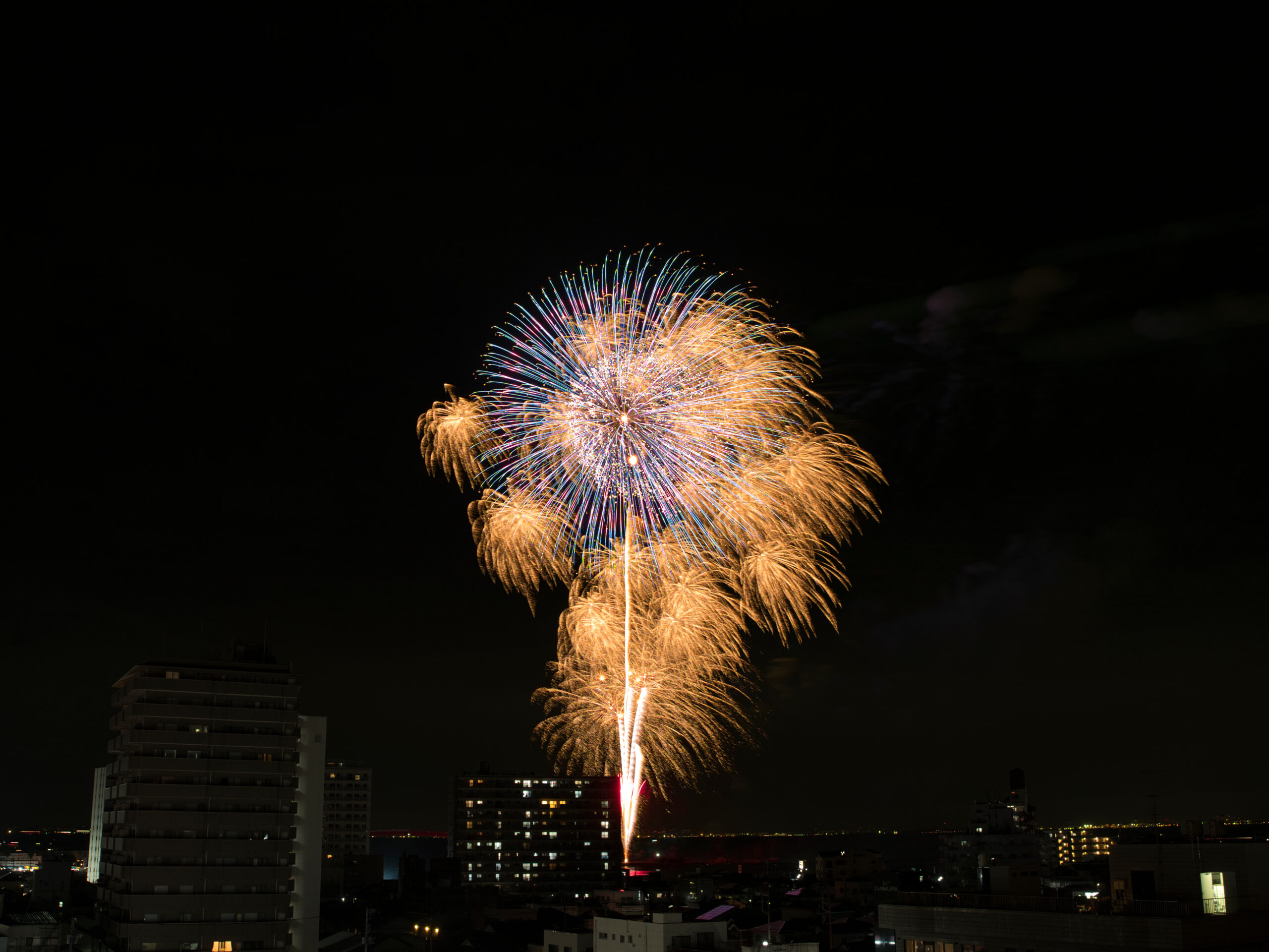 Colorful fireworks explode above a dark city skyline, illuminating tall buildings at night.