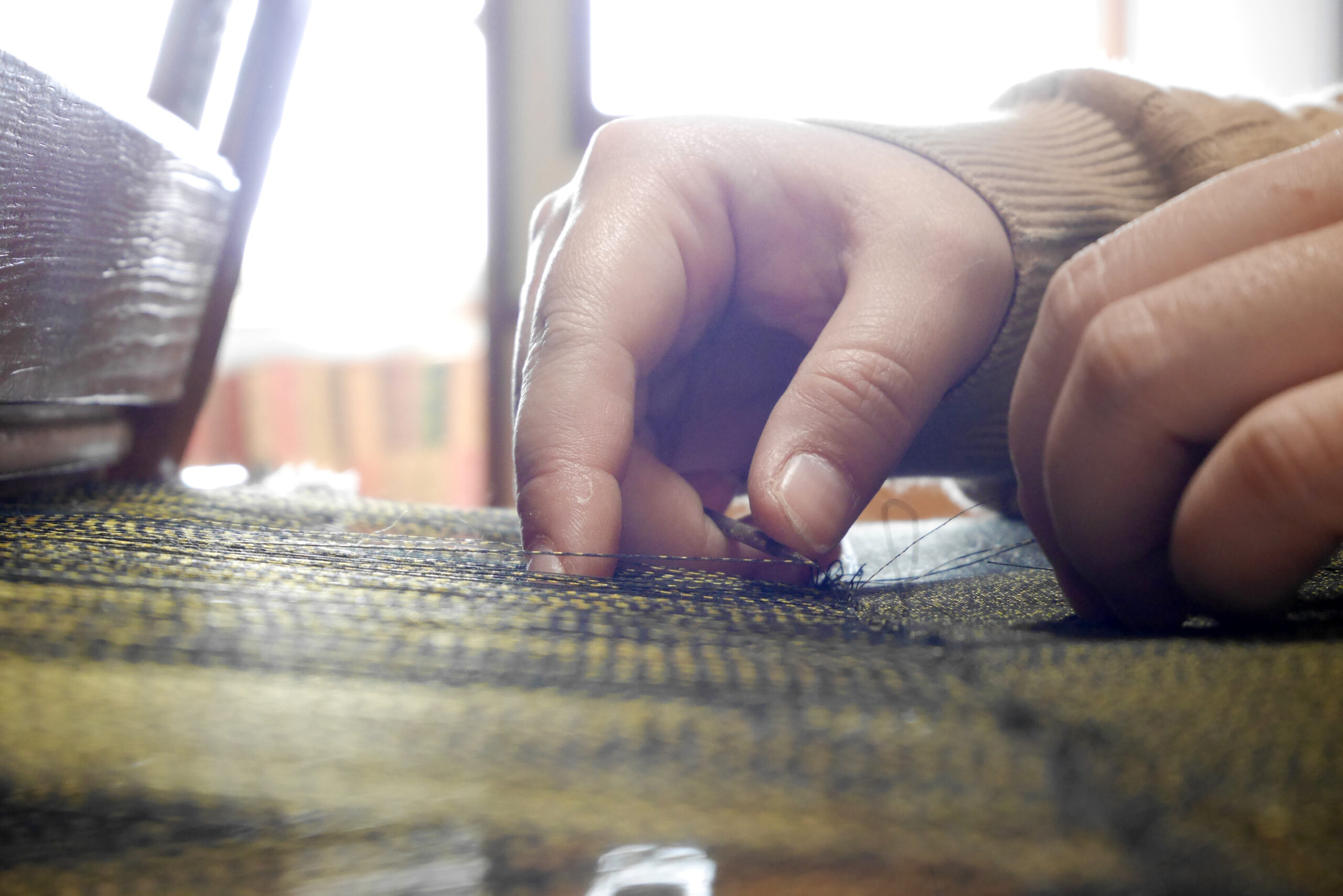 Close-up of hands sewing with a needle, threading dark denim fabric.