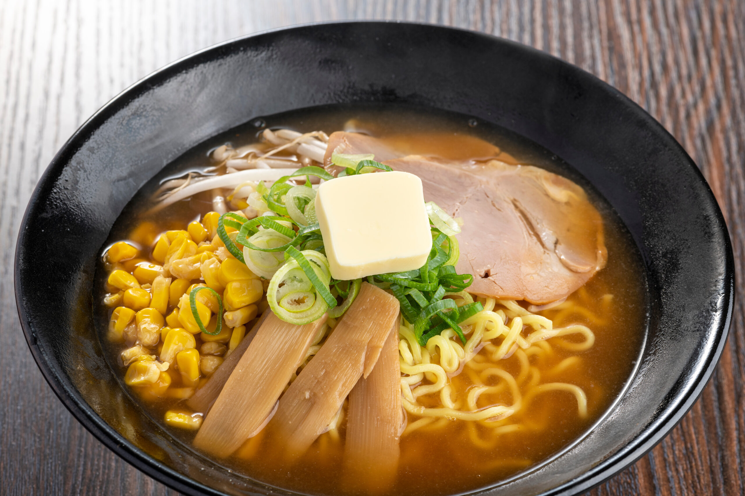 Bowl of ramen topped with corn, sliced pork, green onions, bamboo shoots, and a pat of butter in broth