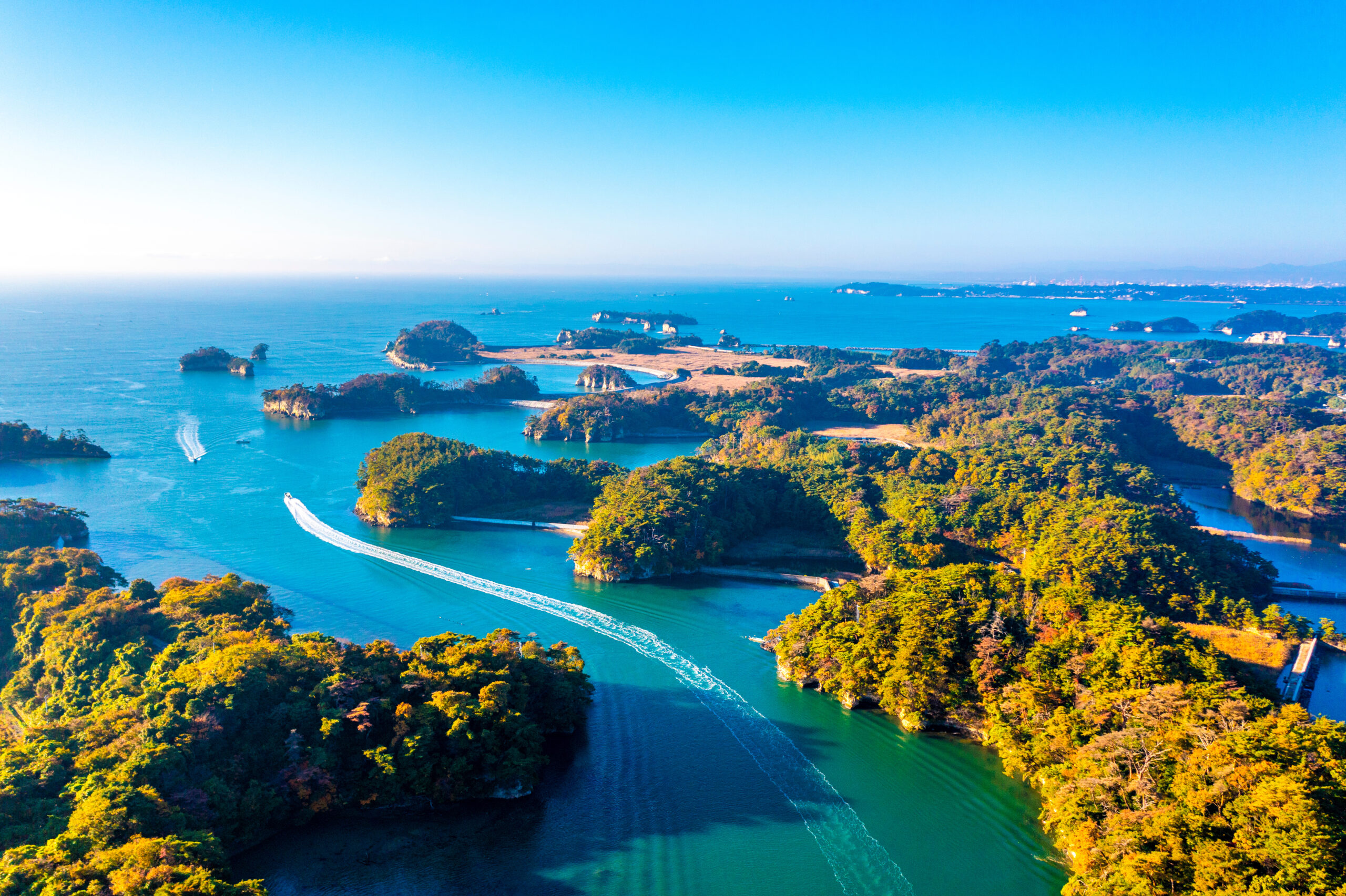 Aerial view of a blue sea with small forested islands and a winding waterway under a clear sky.