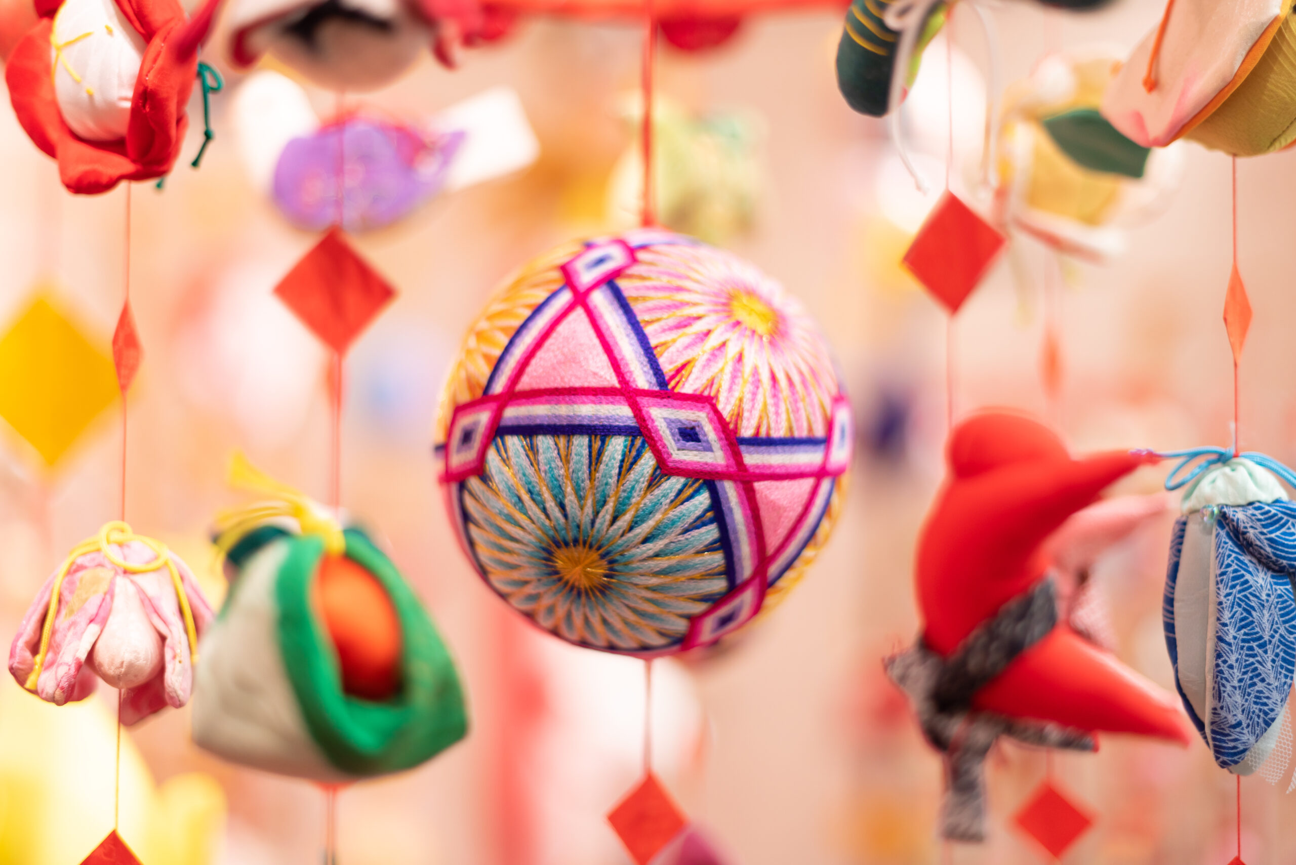 Close-up of colorful hanging decorative ornaments in pink, red, yellow, and teal against a warm background read as festive decor