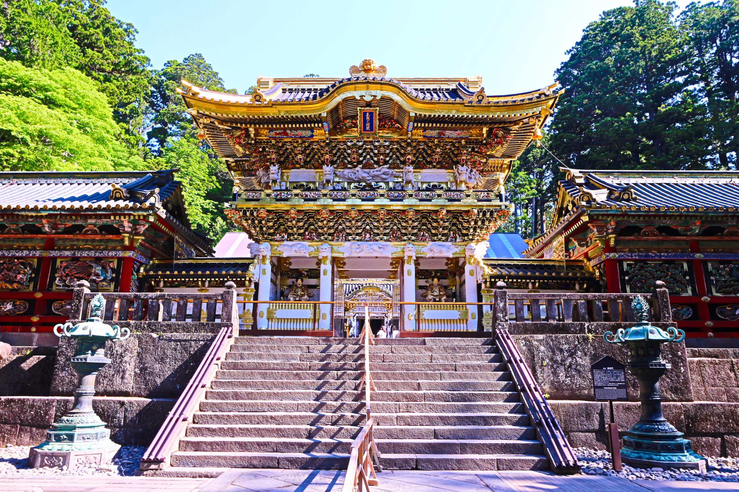 Ornate temple façade with gold detailing and multiple tiers, set among green trees at the entrance steps.