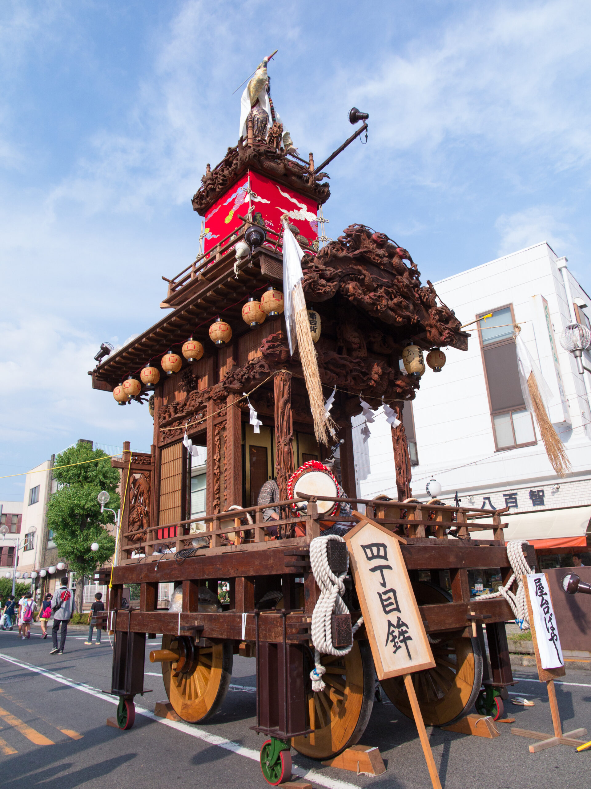 Ornate wooden festival float with carved dragons, a red panel, and hanging lanterns on a city street.