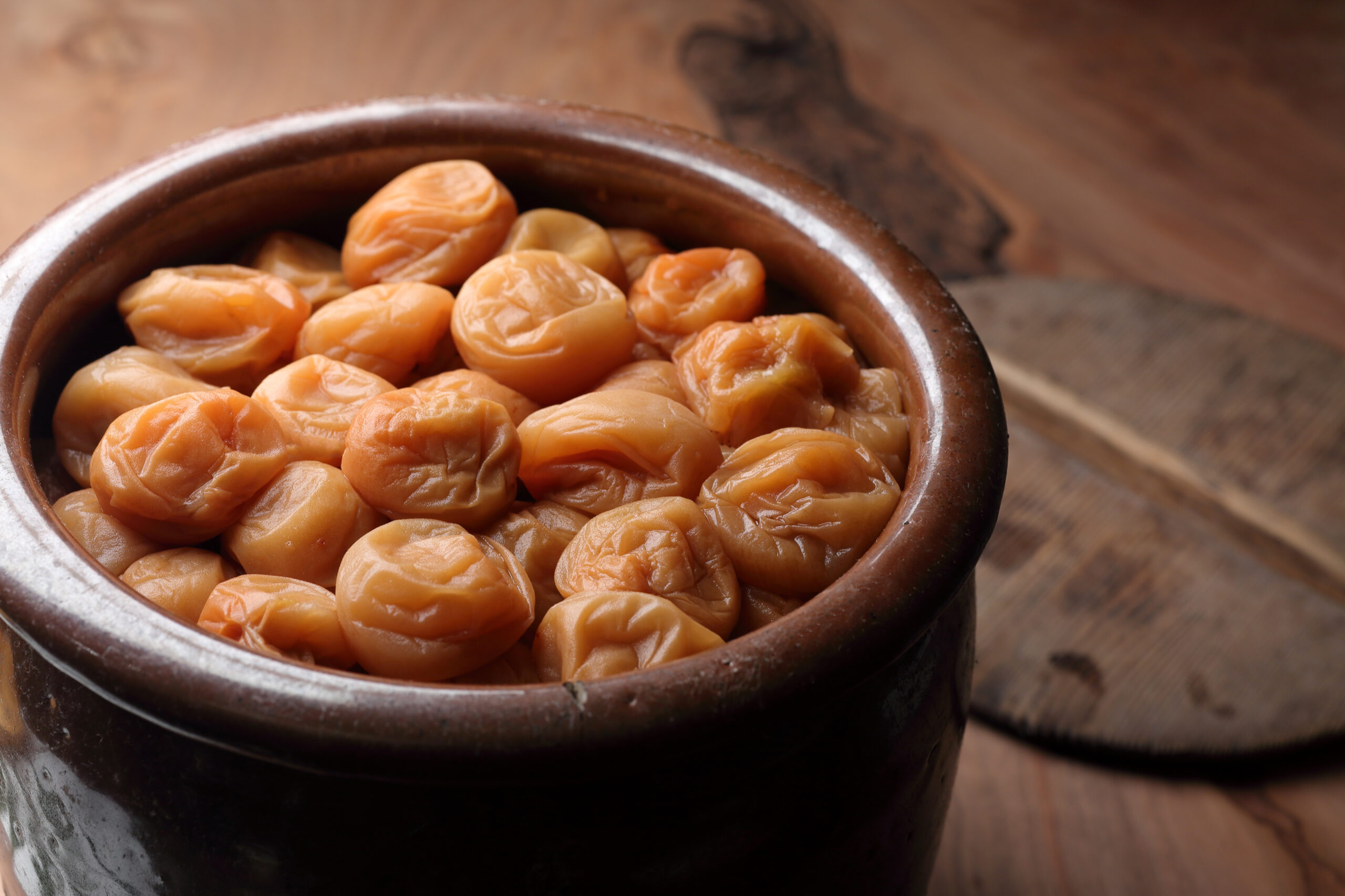 Clay pot filled with orange dried apricots on a wooden table, close-up view.