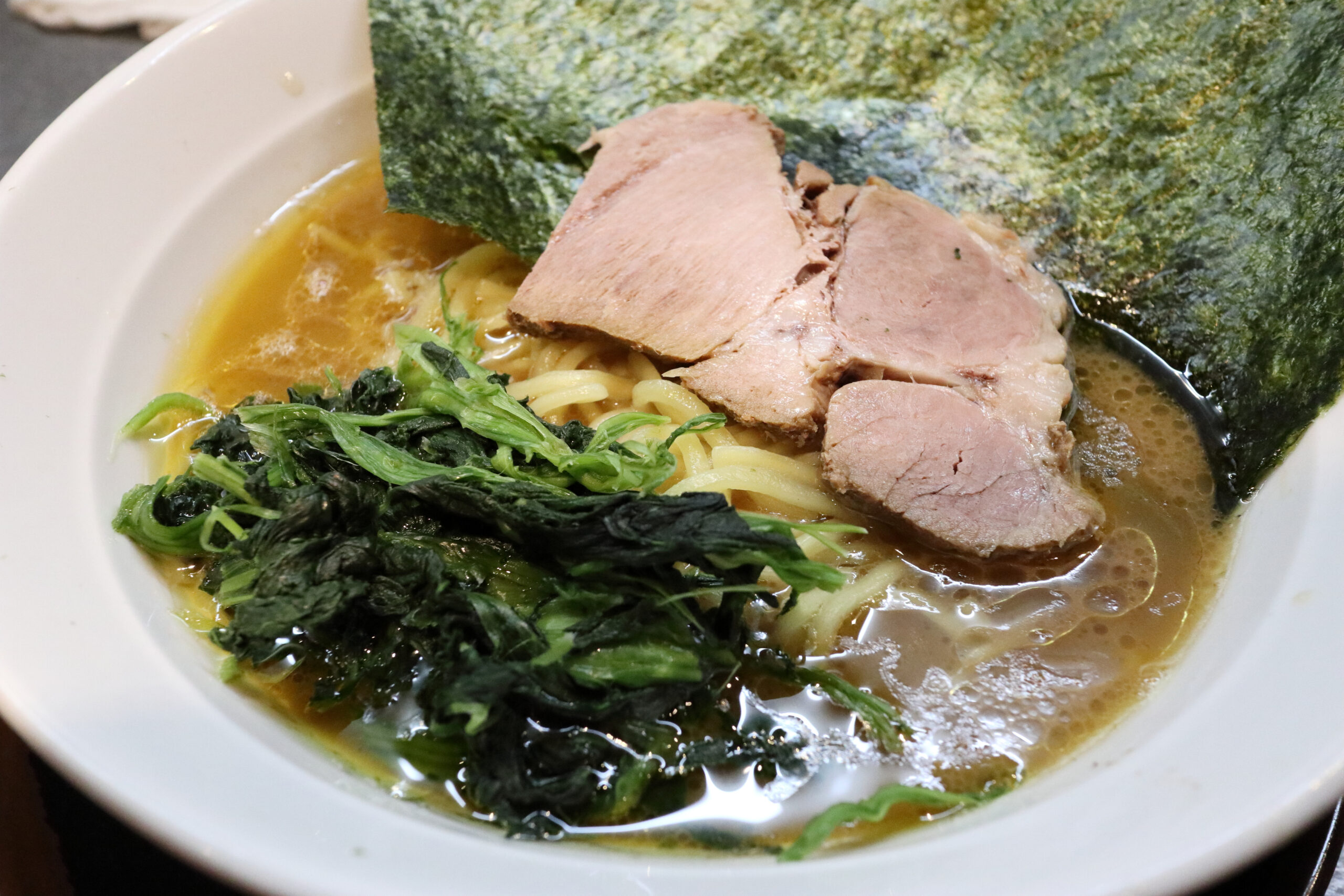 Ramen bowl with sliced pork, greens, seaweed, and rich broth close-up
