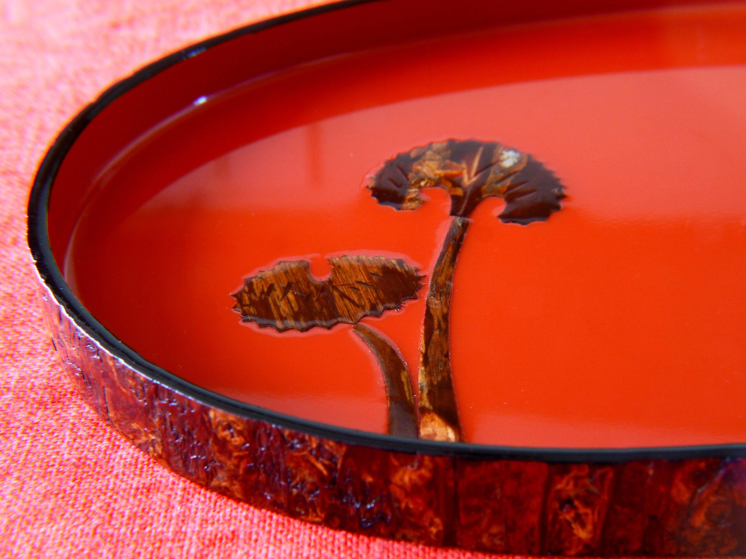 Close-up of a glossy red guitar body with a dark circular soundhole border and a wooden bridge, resting on pink fabric.