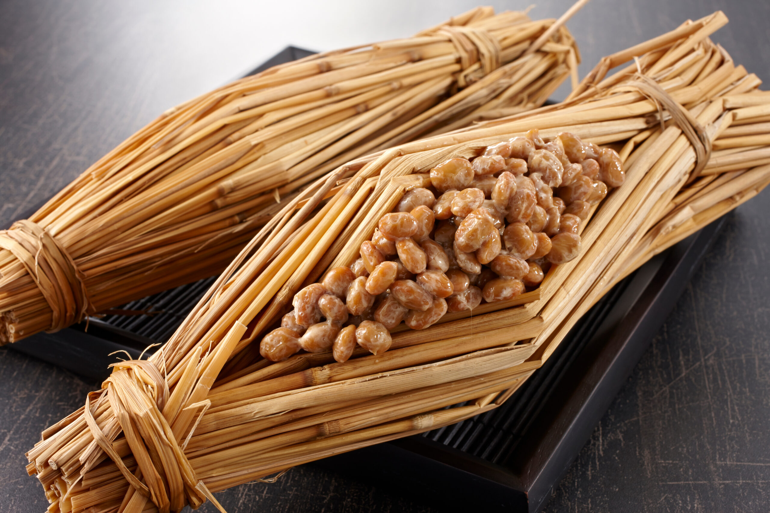 Close-up of straw-wrapped bundles tied with twine, with brown roasted beans spilling from one bundle on a dark surface