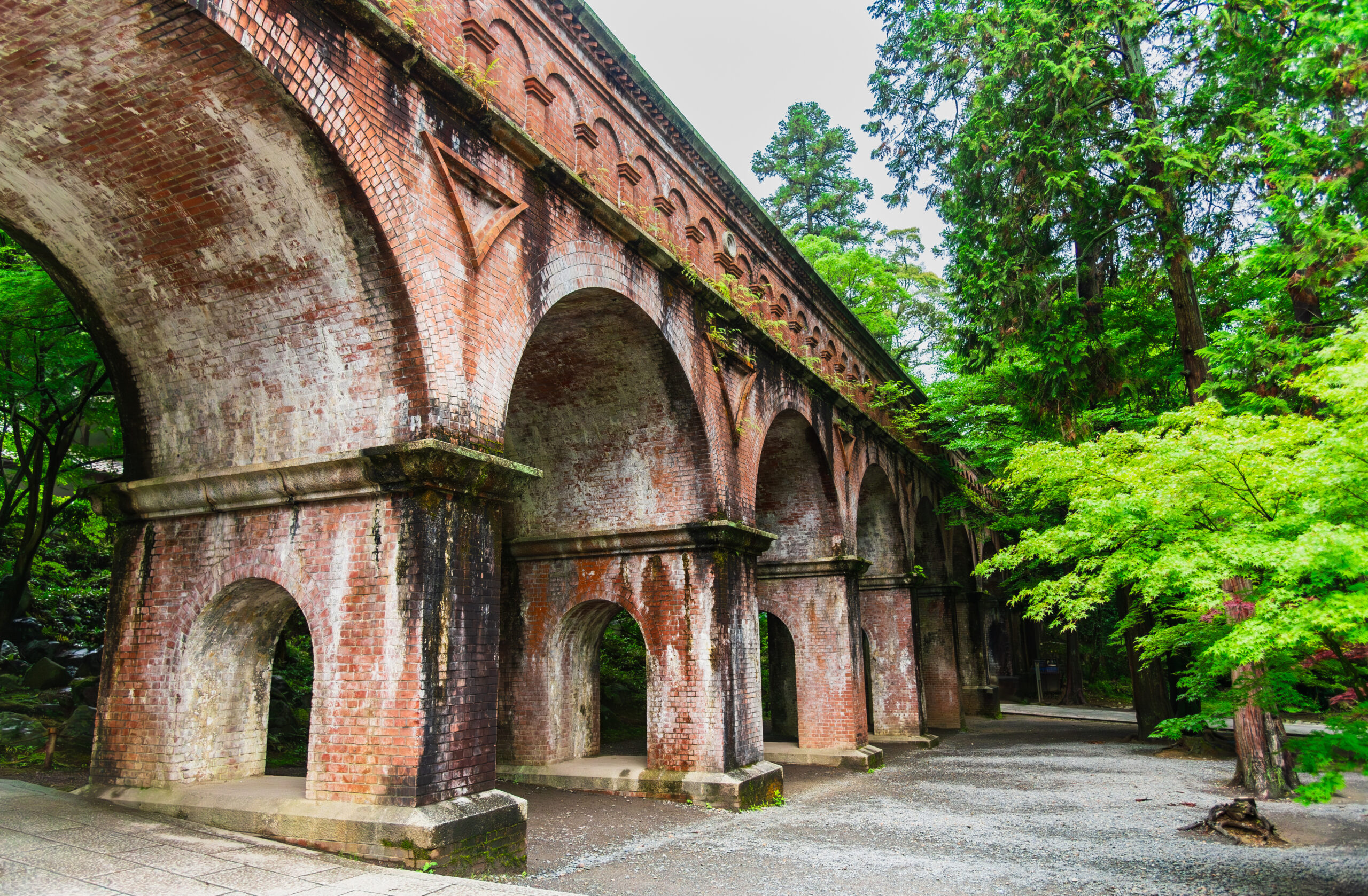 Brick aqueduct with a row of arches fading into a green forest. Mossy, weathered stonework.