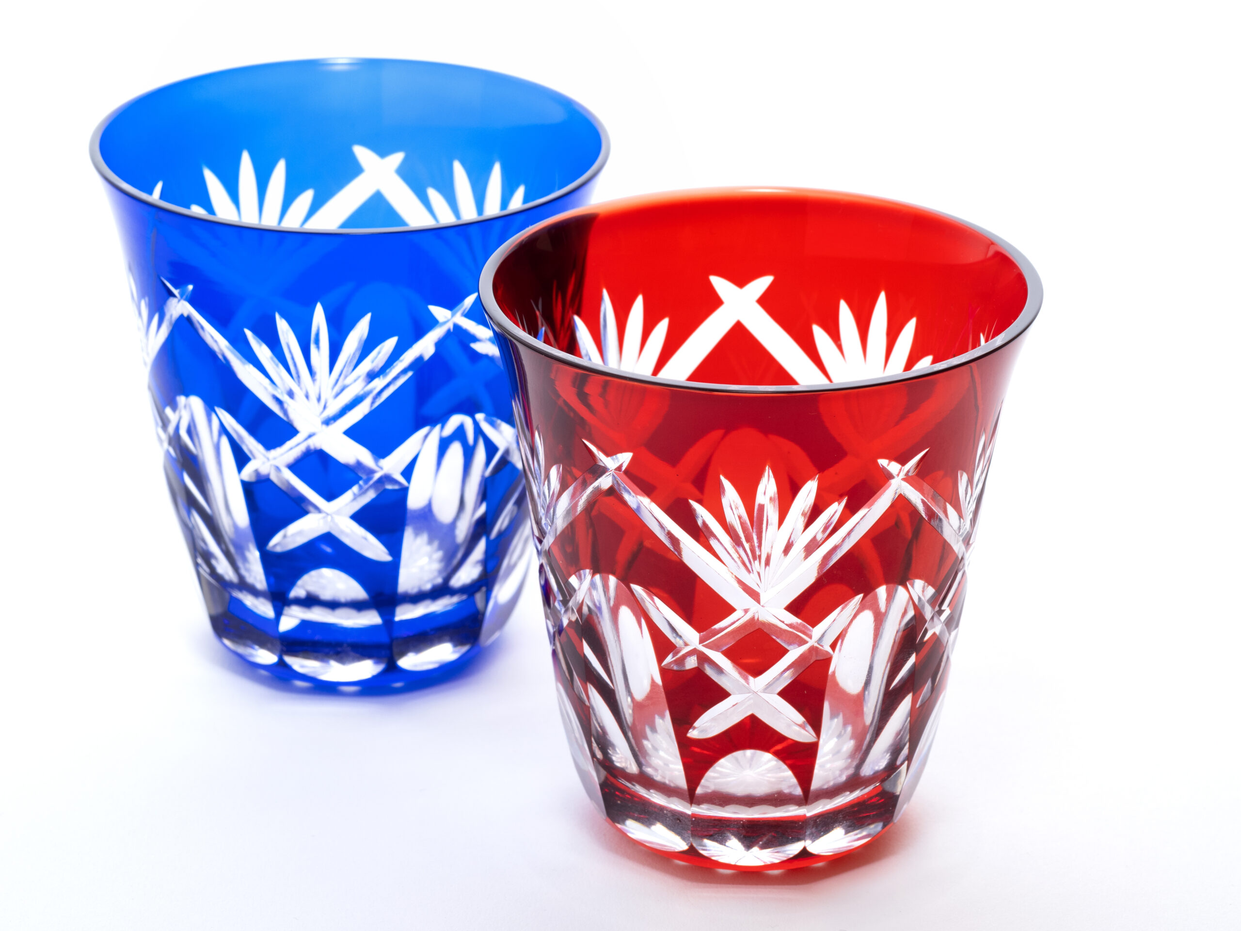 Two cut-crystal tumblers, blue and red, with white starburst patterns on a white background.