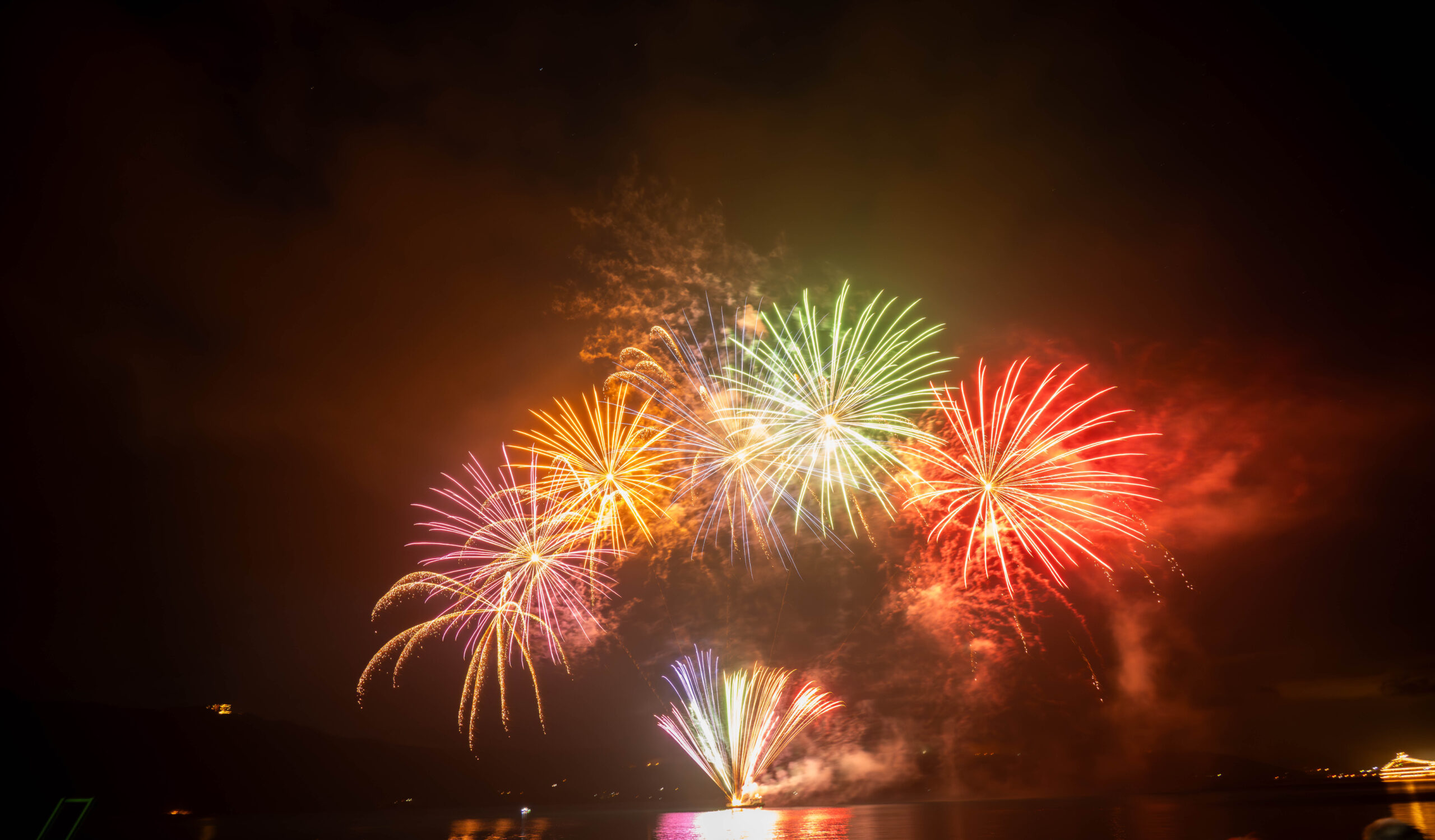 Colorful fireworks bursting over a dark night sky with reflections on calm water.