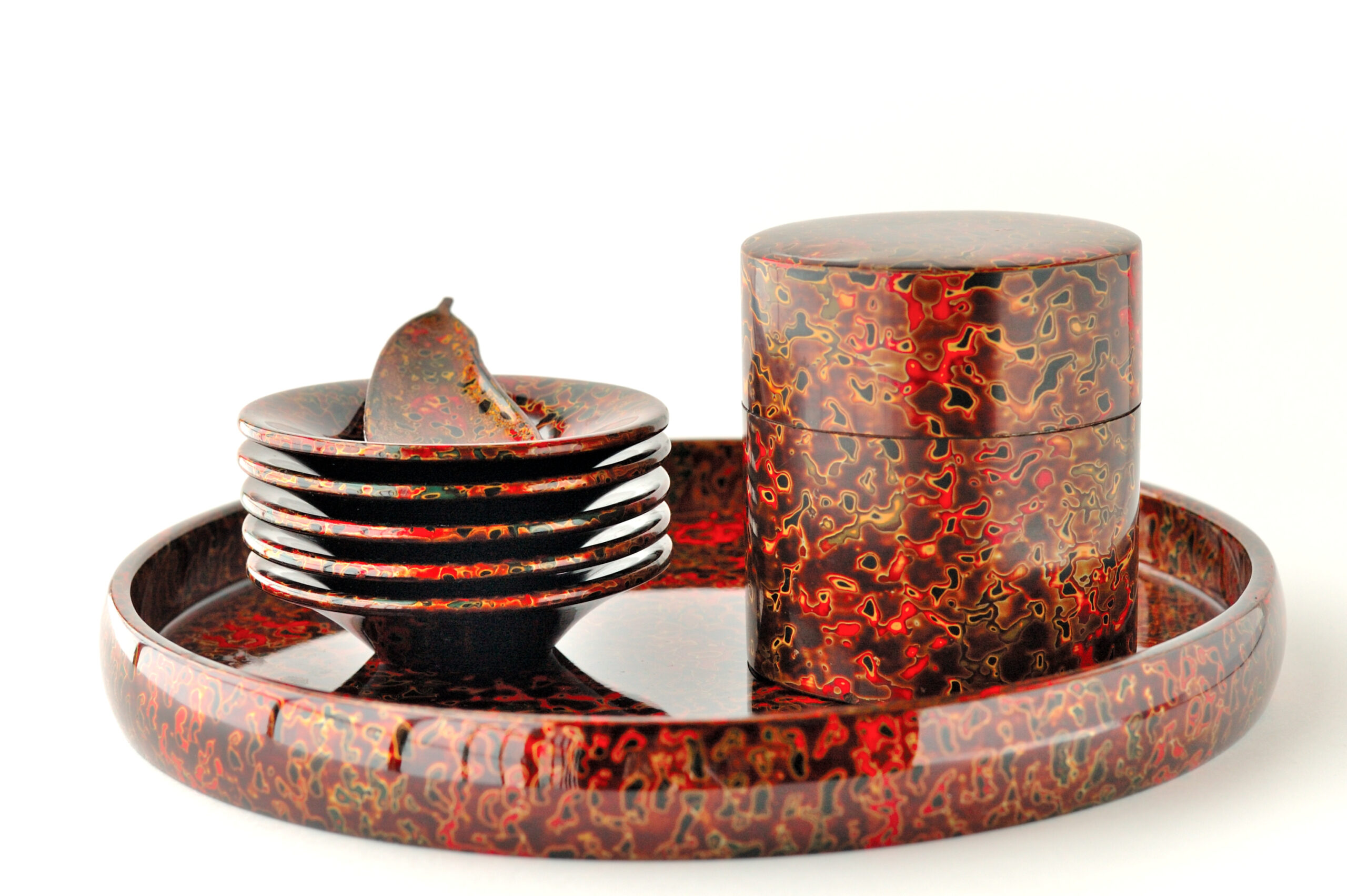Close-up of a red marbled lacquer dinnerware set: nested shallow bowls on a round tray with a tall lidded container nearby.