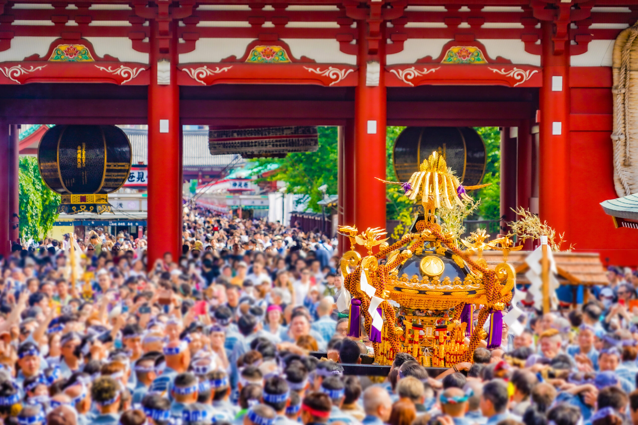 Crowd at a Japanese festival with an ornate golden mikoshi float in the foreground and red temple gates above.