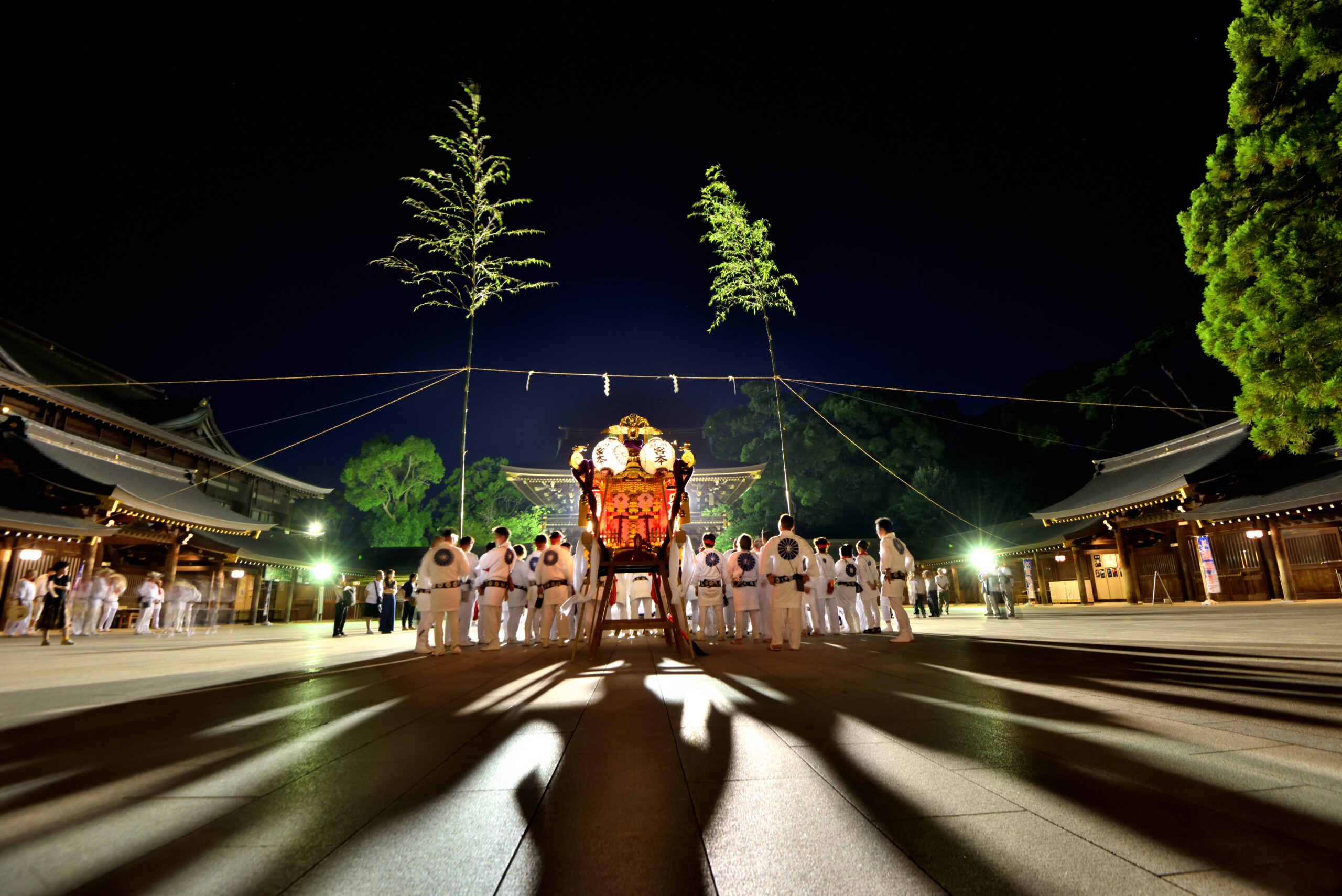Night festival at a temple courtyard with a decorated portable shrine surrounded by people in white robes.