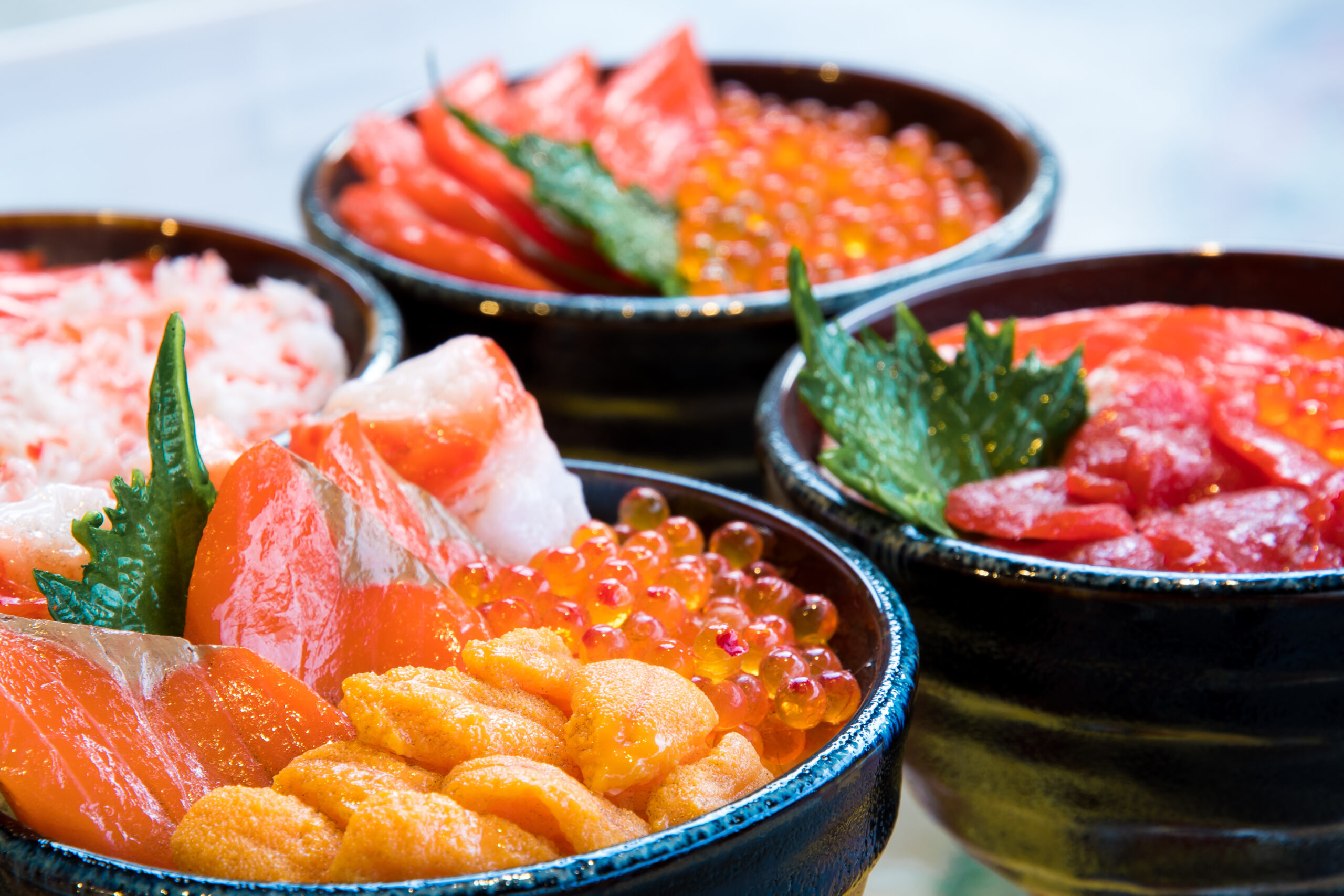 Assorted seafood bowls with salmon sashimi, salmon roe, and greens in blue ceramic bowls.
