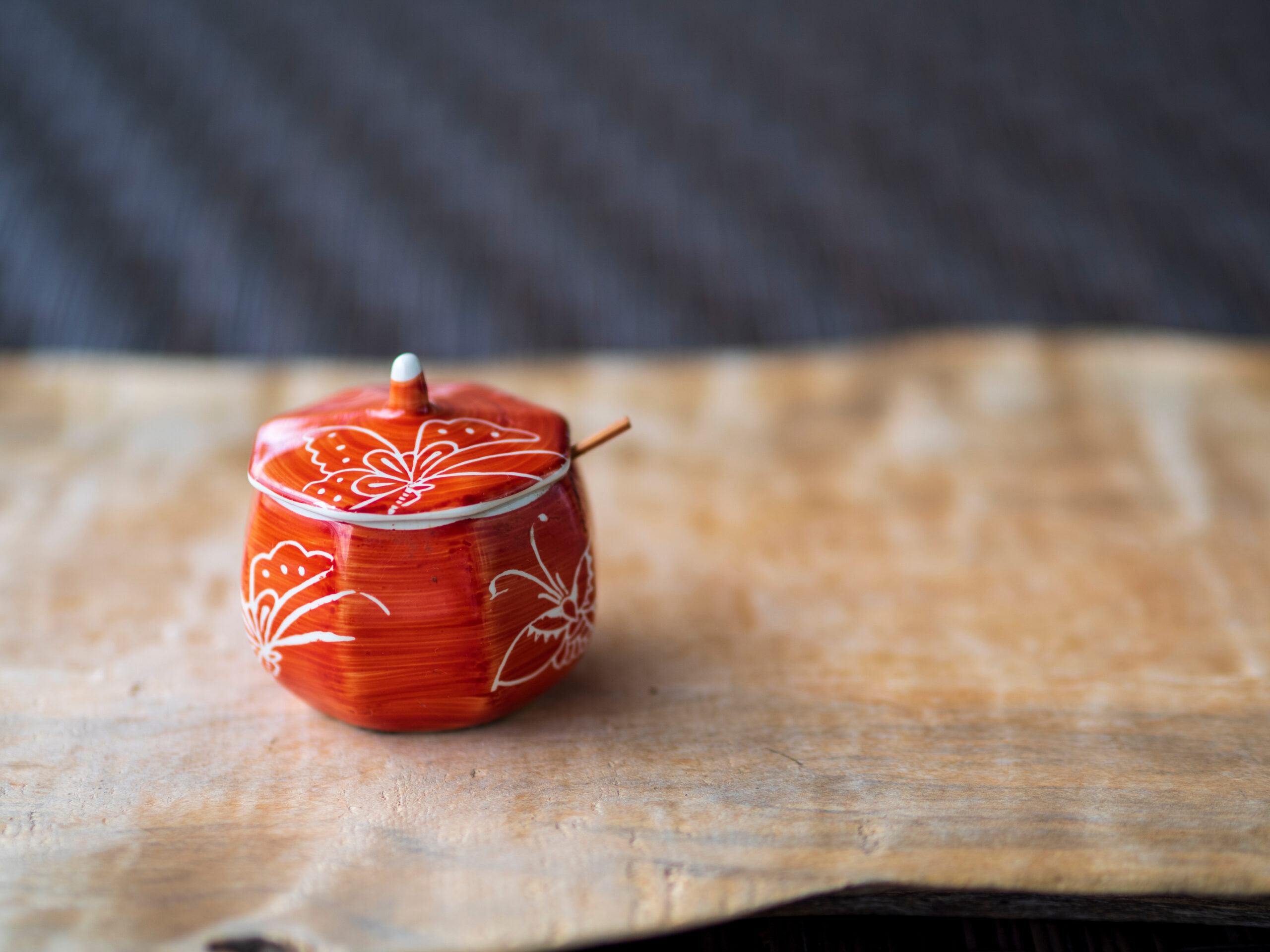 Close-up of a red ceramic teapot with white floral patterns on a wooden table.