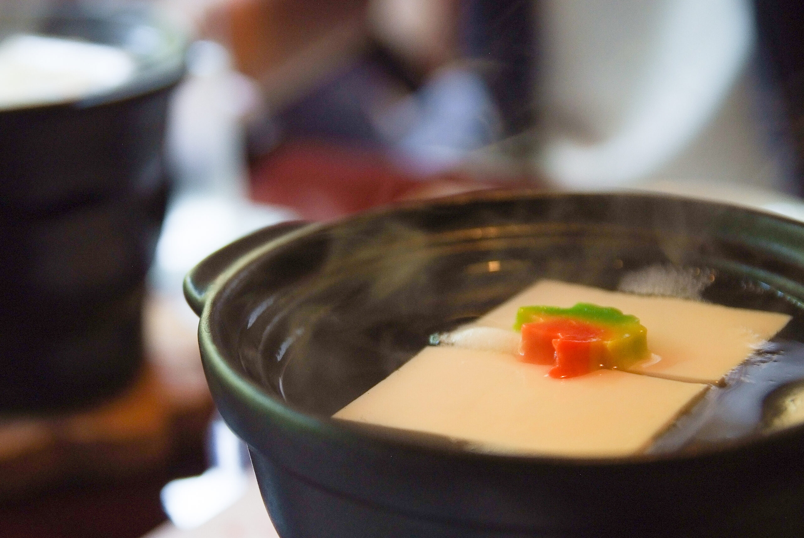 Close-up of a dark ceramic bowl holding a white dessert topped with small multicolored candy pieces (green, red, orange).